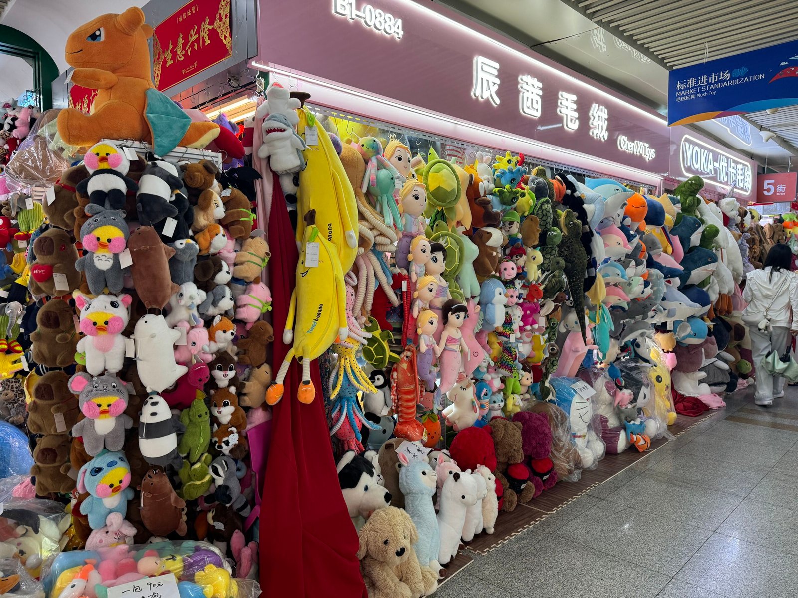 Colorful plush toy and stuffed animal display at a wholesale vendor stall in Yiwu International Trade Market, China. The shop features hundreds of cute stuffed animals including teddy bears, pandas, cartoon characters, and novelty plush toys arranged from floor to ceiling, showcasing the diverse wholesale toy offerings available at the world's largest small commodity market. Plush toy is a good item for dollar store.