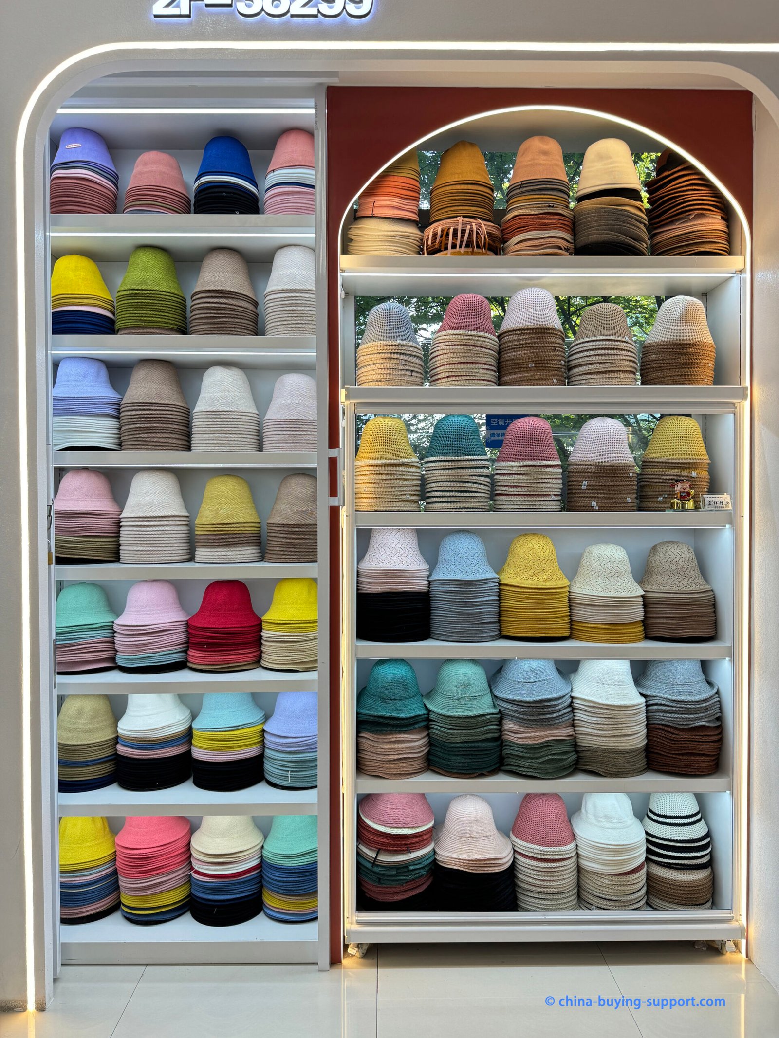 Factory sample showroom with well-lit, floor-to-ceiling shelves of color-sorted woven, knitted and cotton bucket hats for bulk purchase.