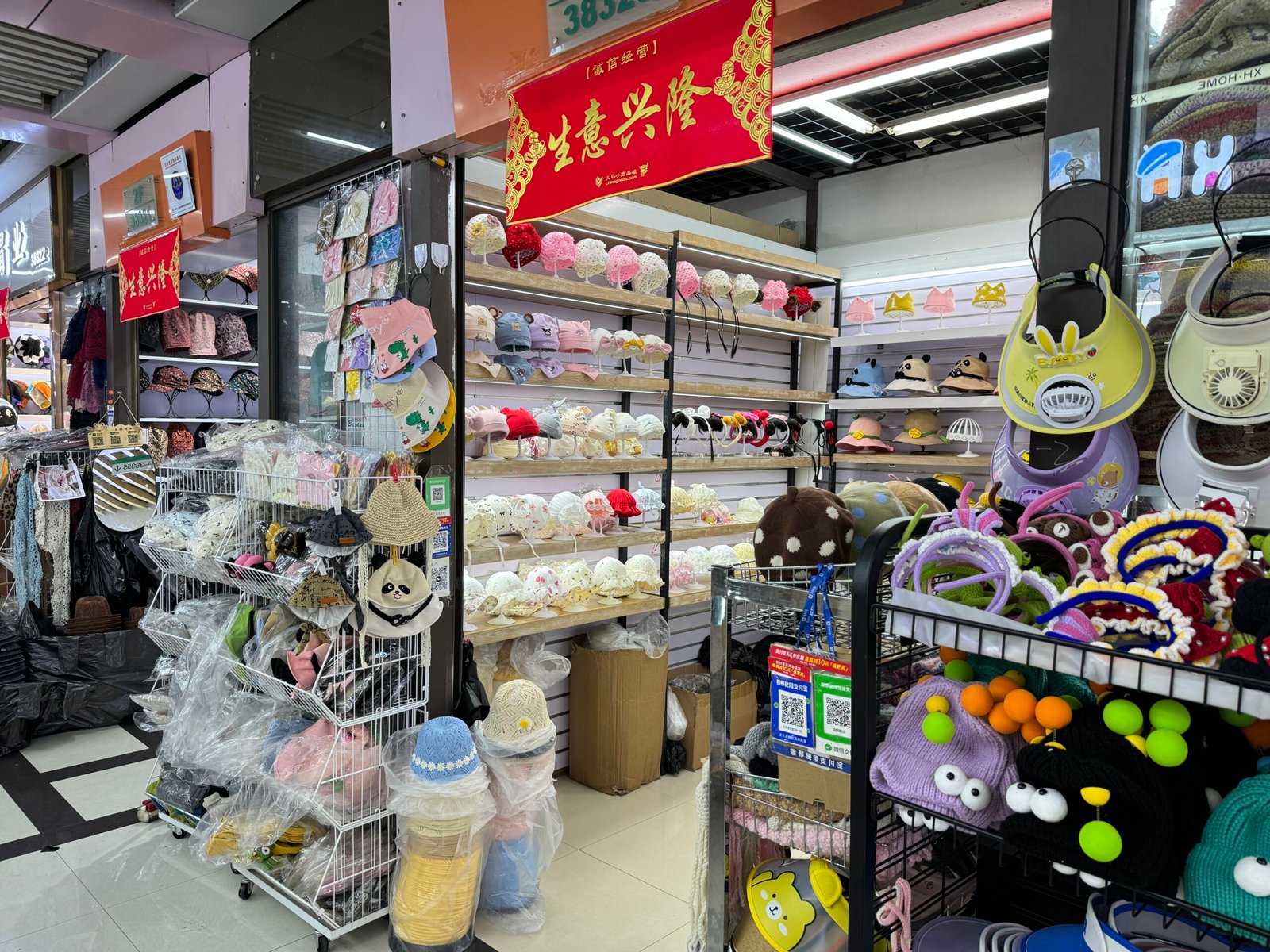 Shelves of baby lace bonnets, crown headbands, panda bucket hats and toddler sun hats at a wholesale shop in Yiwu International Trade Market