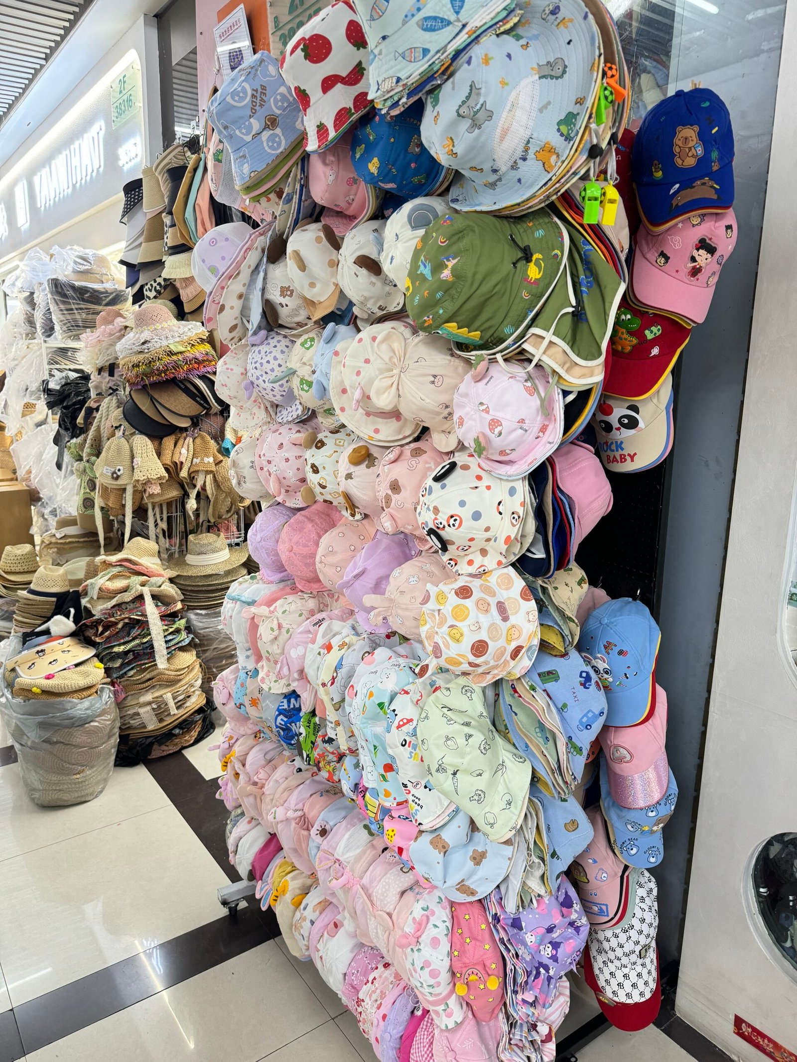 Rack of baby and toddler sun hats at Yiwu Market—printed cotton bucket hats and bonnets with chin straps in pastel colors