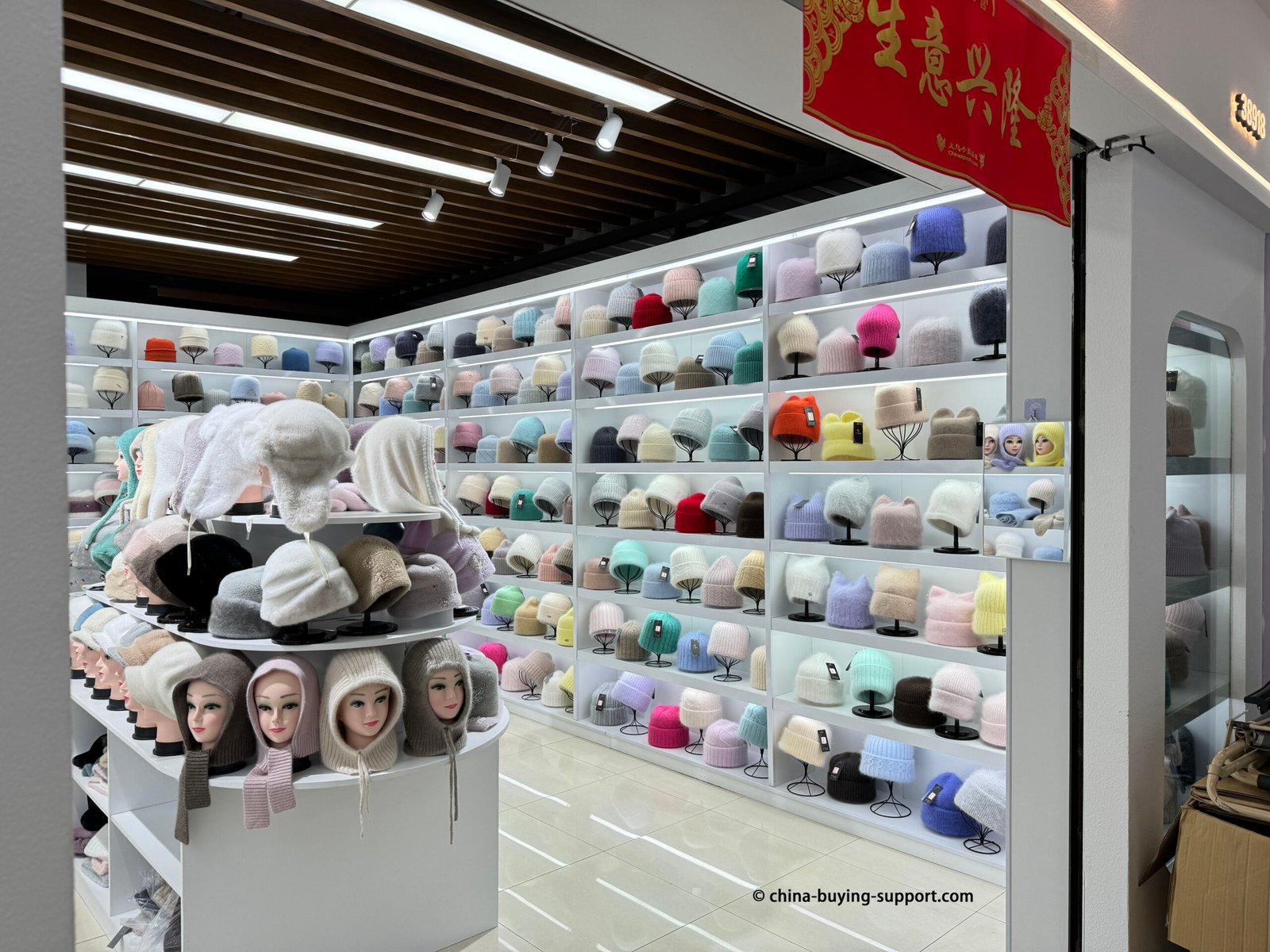 Yiwu hat market display with pastel, neon and neutral knitted beanies on white backlit shelves in China