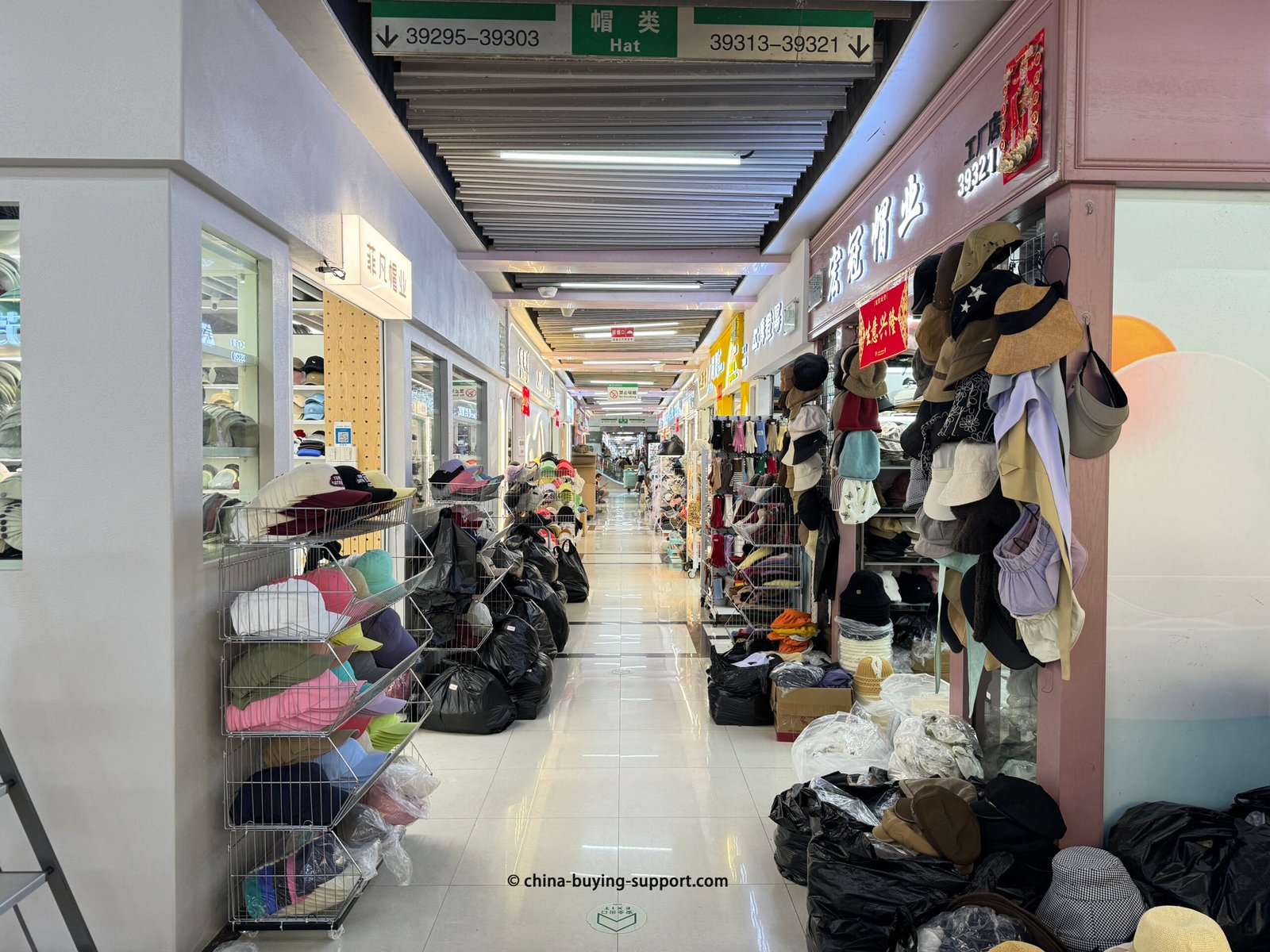 Aisle inside Yiwu International Trade City’s hat section, with wholesale shops selling bucket hats, baseball caps and knit beanies stacked floor-to-ceiling
