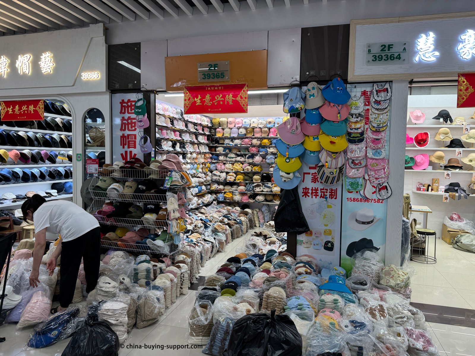 Yiwu hat supplier (2F-39365) focused on ready stock: children’s caps, baby sun visors, bucket hats. Floor-to-ceiling shelves and bagged inventory for fast dispatch.