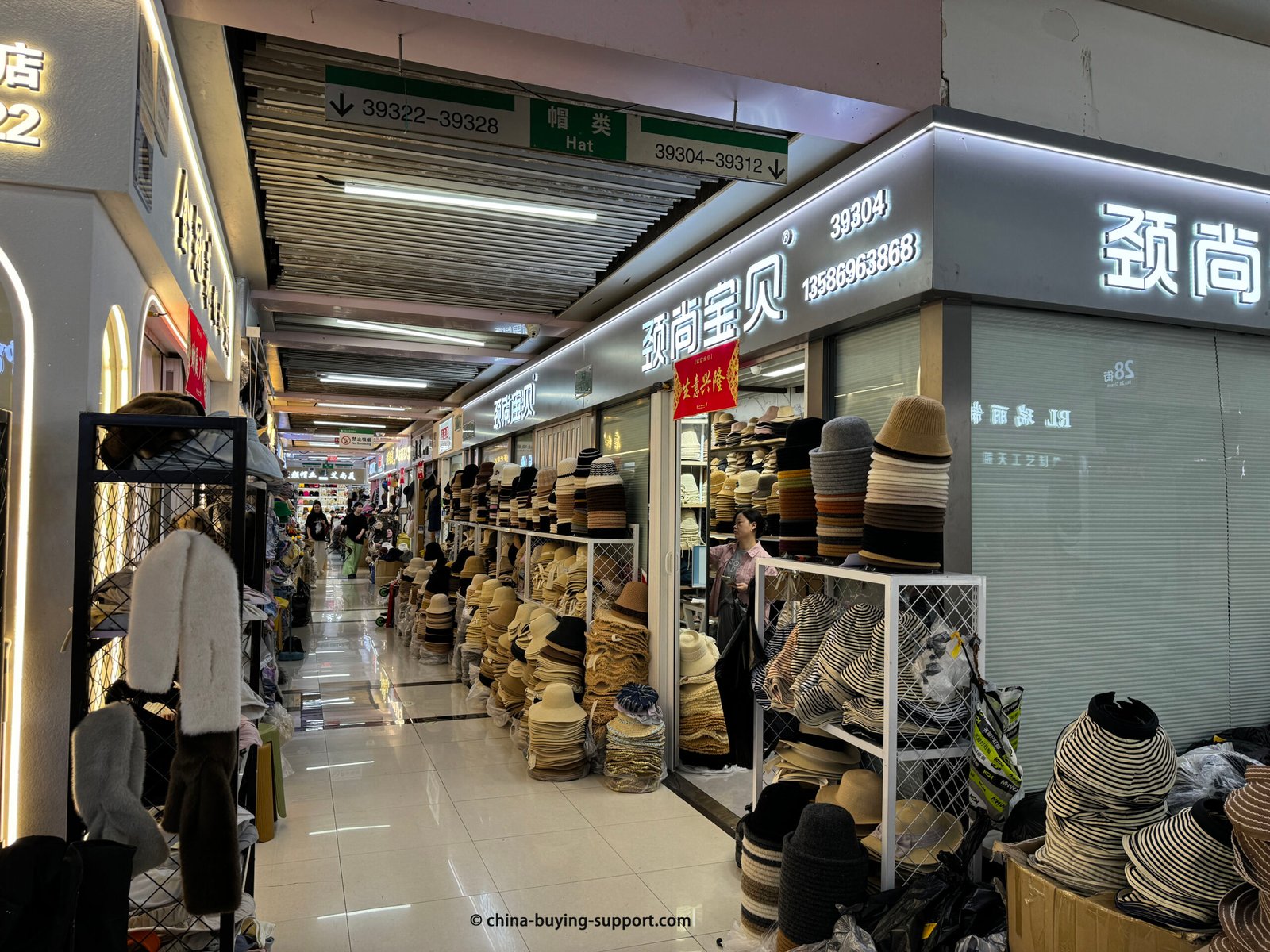 Yiwu International Trade City hat market, shop 39304: stacks of straw sun hats, bucket hats and beanies in a bright wholesale aisle with multiple vendors