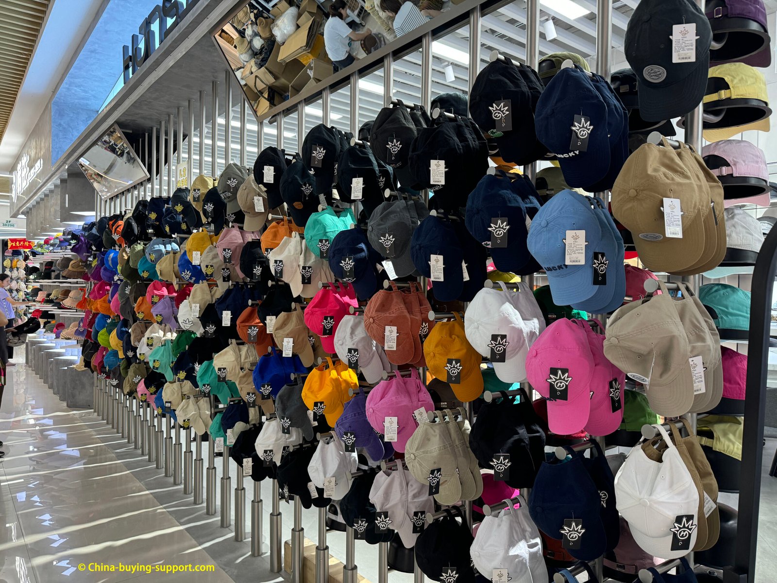 Yiwu Market wholesale wall of colorful baseball caps—cotton twill dad hats with curved brims and strapbacks, arranged by color on metal racks.