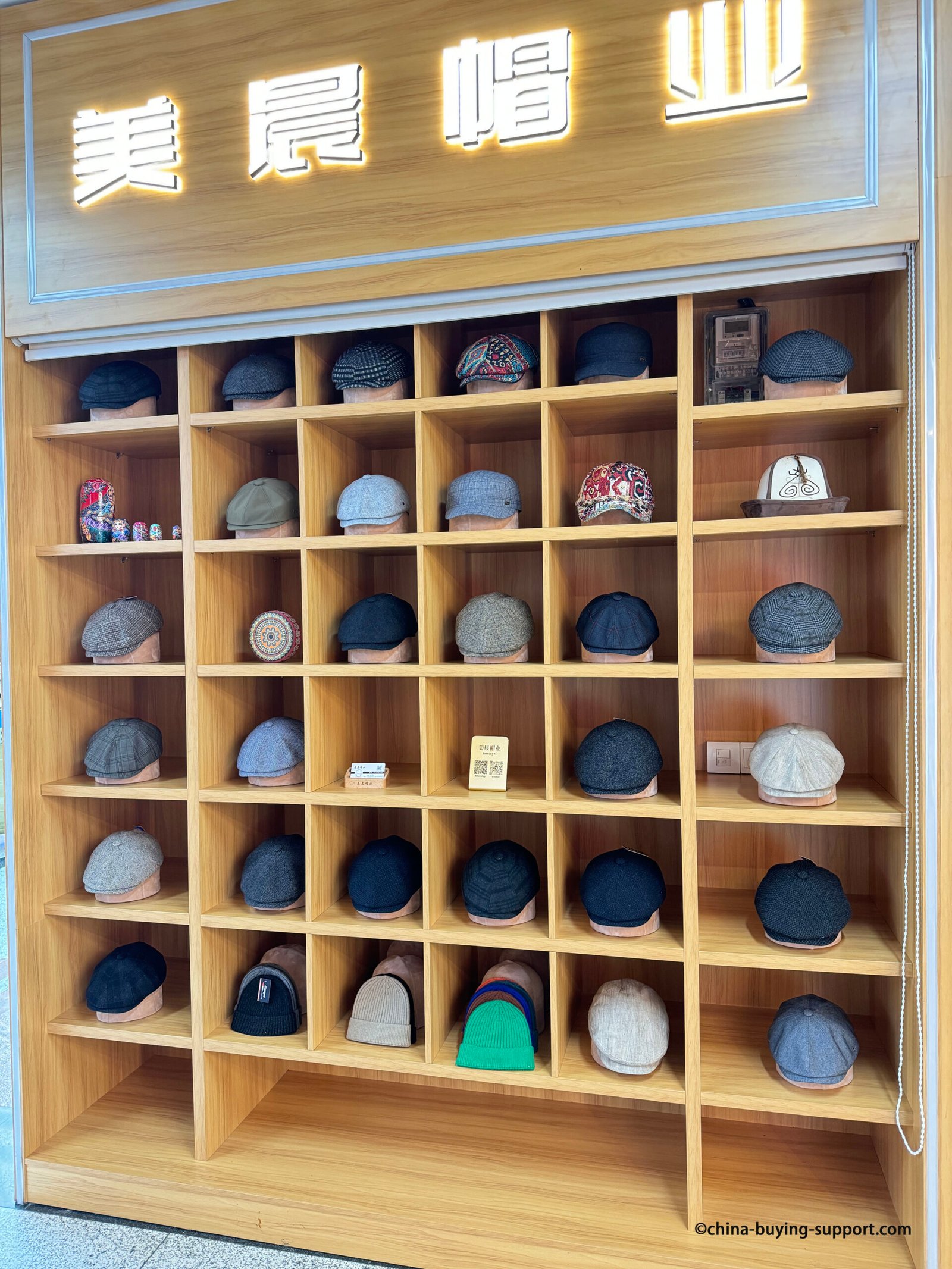 Neat wood cubby shelves at Yiwu Market hat section with men’s flat caps/newsboy–ivy caps in tweed, herringbone, plaid and solid wool tones, plus rib-knit beanies, China