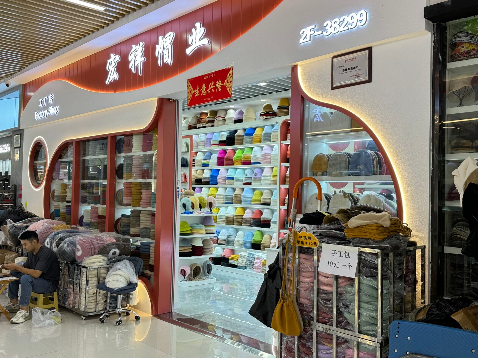 Wholesale hat factory shop at Yiwu Market with walls of colorful beanies, bucket hats, and knit caps, Booth# 2F-38299.