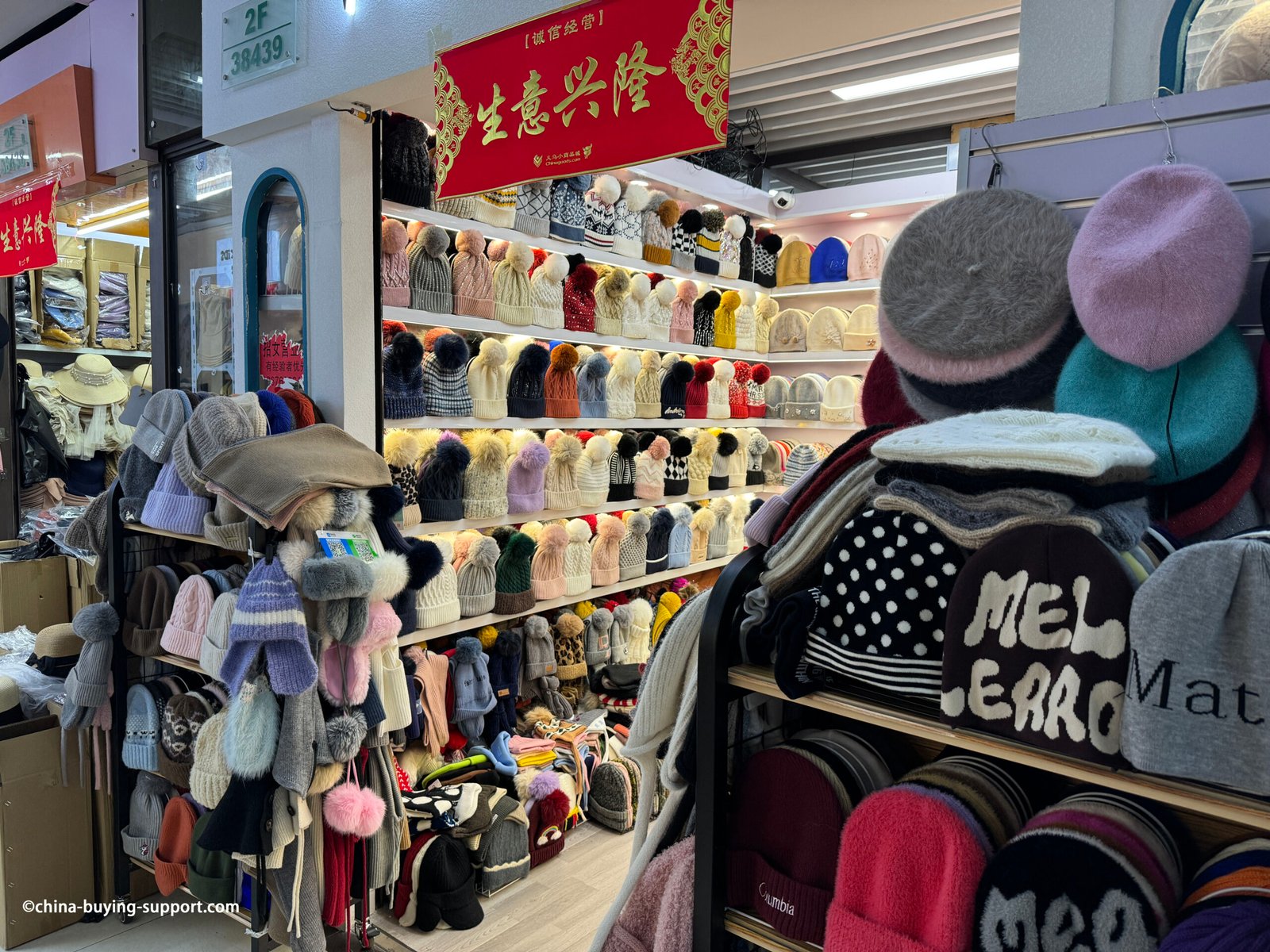 Rows of knitted winter beanies with large faux-fur pom-poms—cable knit, ribbed and patterned—in beige, cream, pink, navy and grey at the Yiwu Market hat section, China