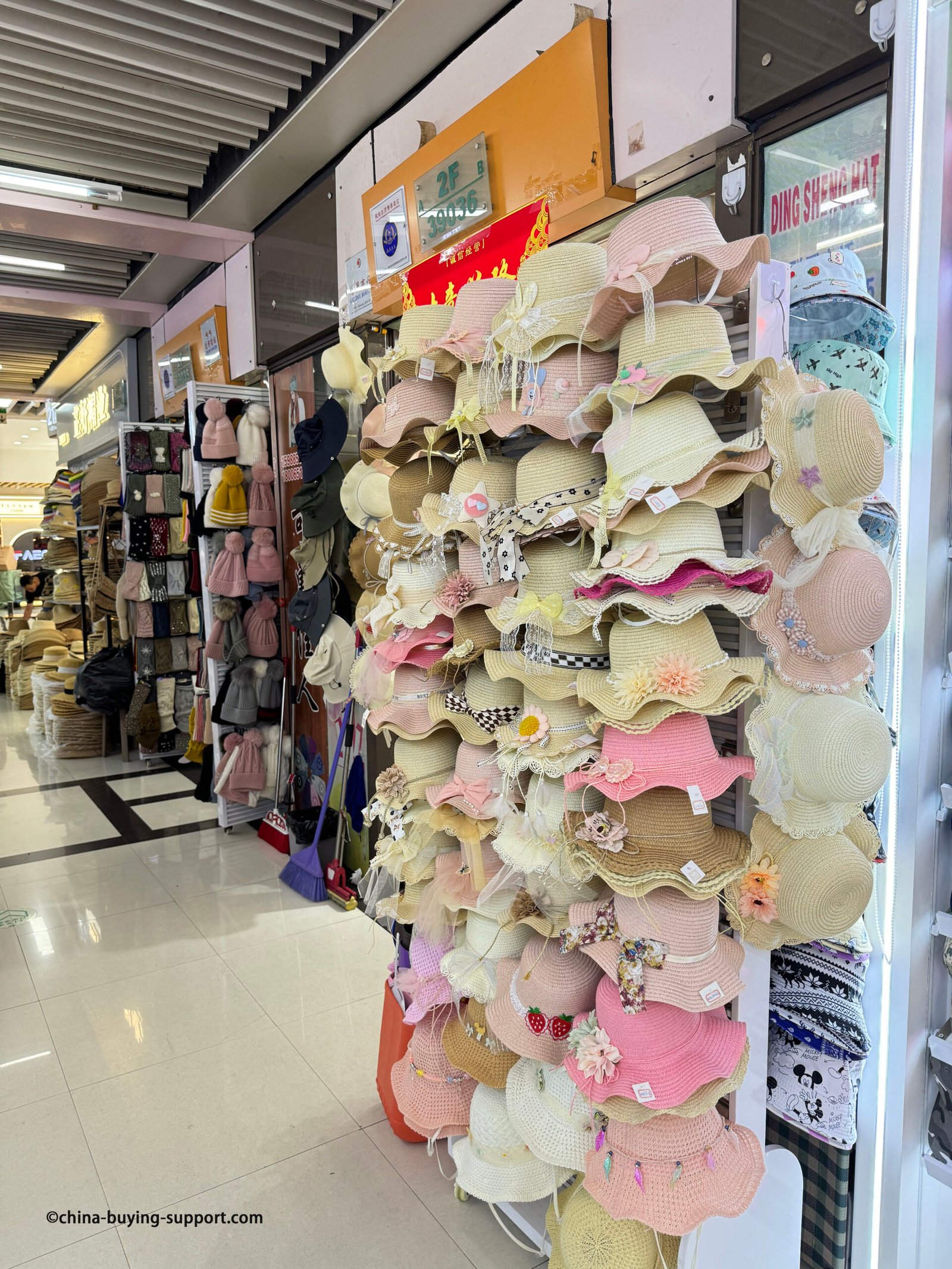Stacked display of pastel woven straw sun hats with scalloped/ruffled brims, lace trim, chiffon ribbons, floral appliqués, bows and checkered bands at the Yiwu Market hat section, China