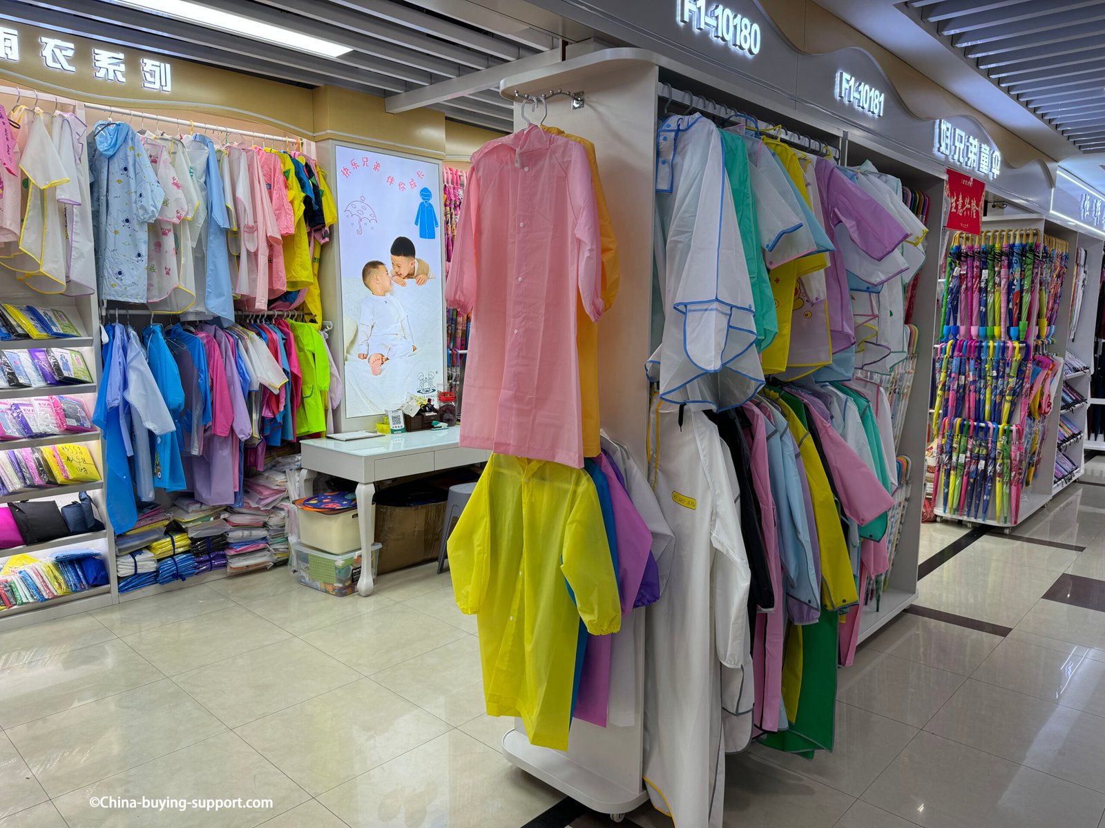 yiwu district 2 kids raincoats wholesale shop interior with pastel and neon ponchos, packaged rainwear, poster display