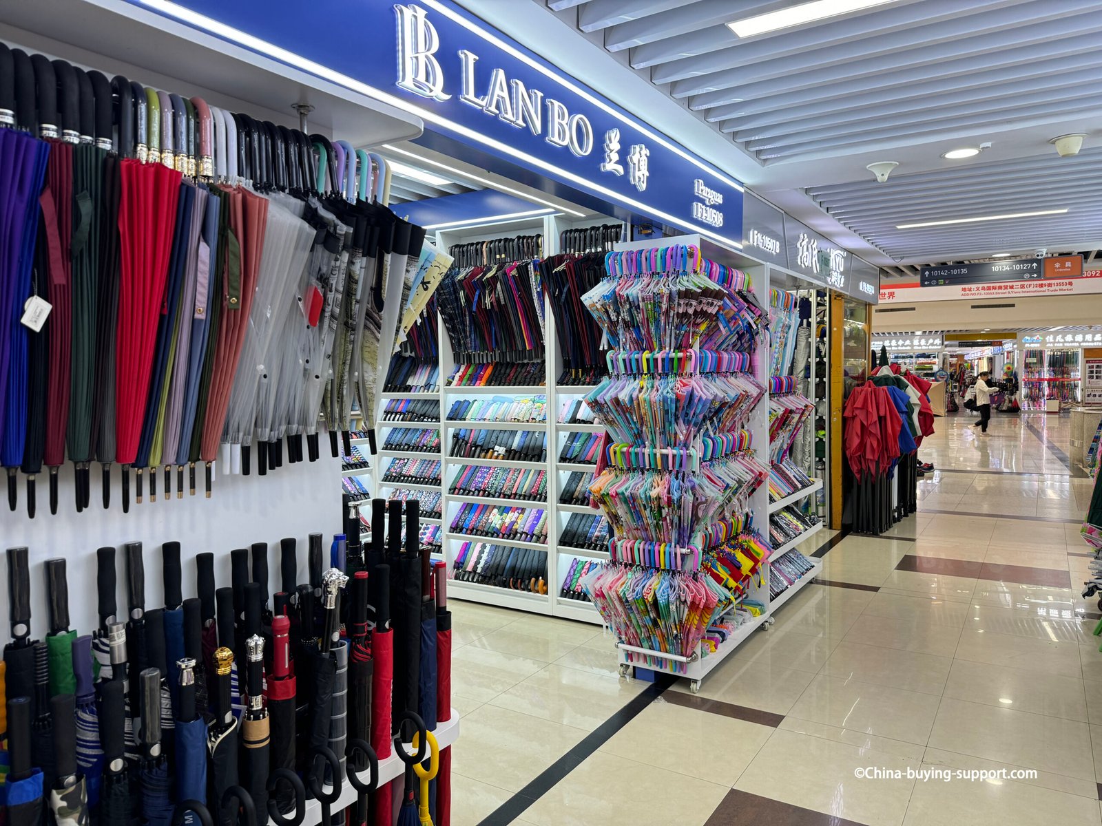 yiwu district 2 LANBO umbrella store interior with long-handle racks, shelves of compact folding umbrellas, carousel of colorful kids umbrellas, bright polished aisle