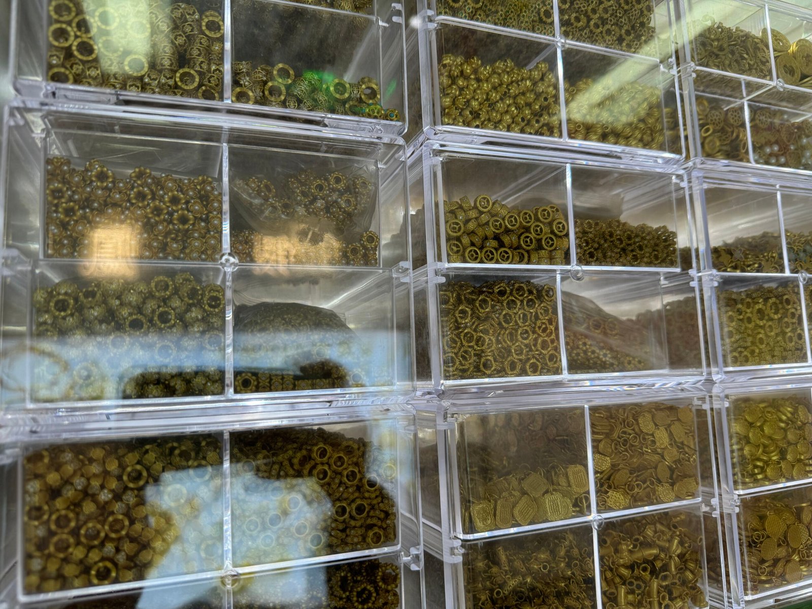Small antique brass spacer beads—rondelle, heishi and gear styles—organized in bins at a Yiwu copper findings supplier.
