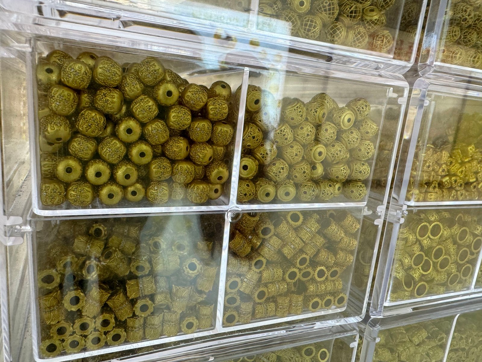 Trays of antique brass filigree round beads and textured square barrels from a Yiwu copper findings supplier.