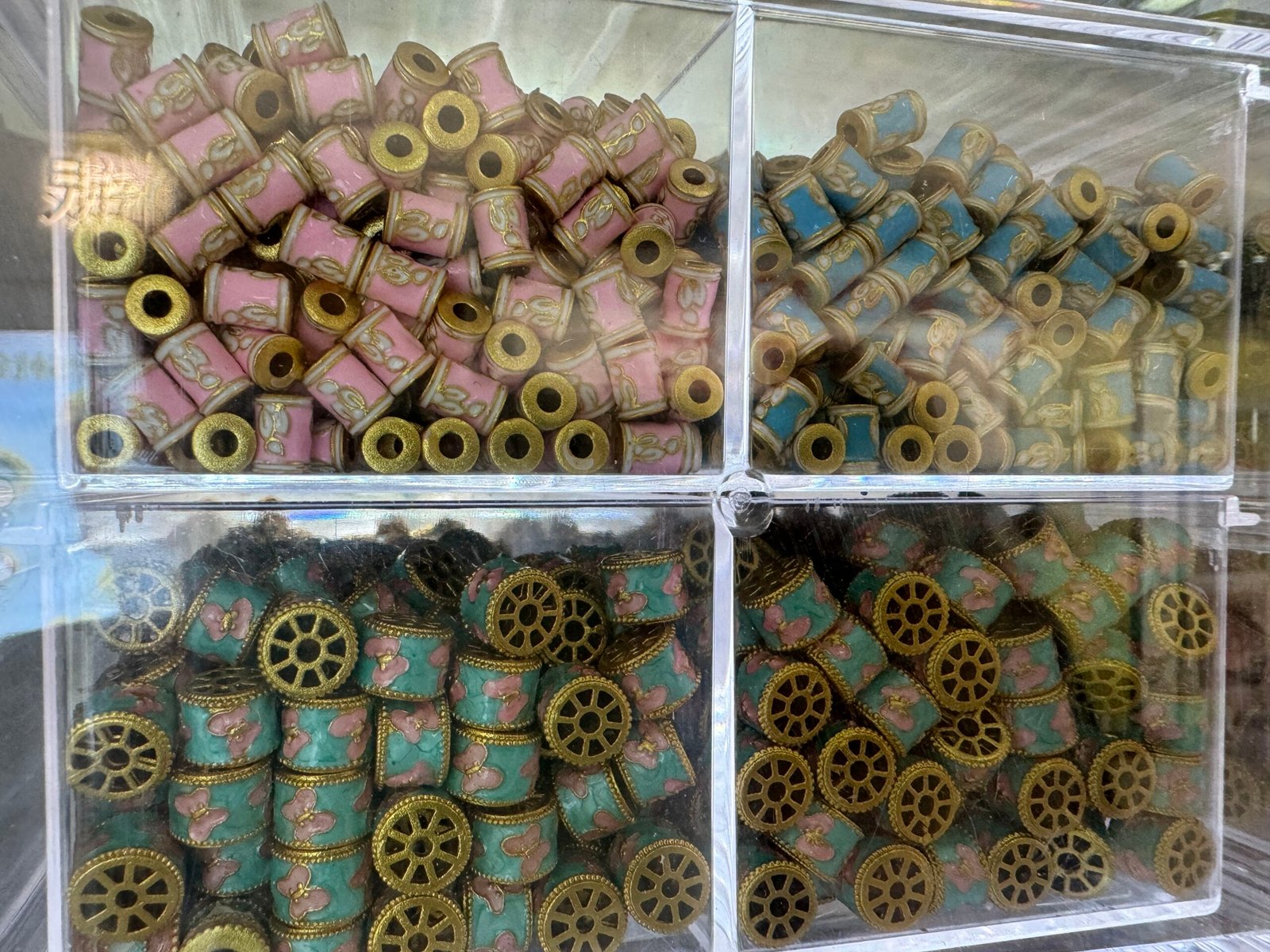 Pastel cloisonné enamel copper barrel beads with floral and butterfly patterns in bins at a Yiwu wholesale shop.