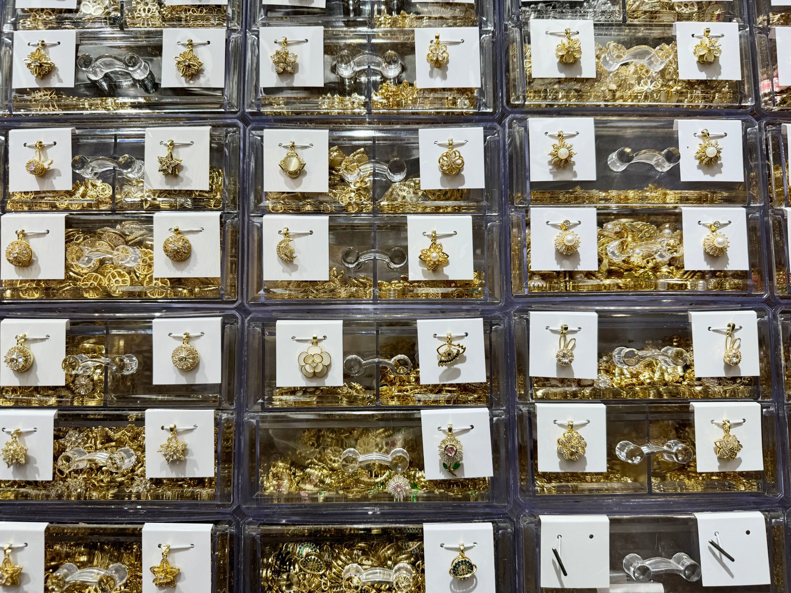 Drawers of gold-plated copper pendants in Yiwu, China, including filigree spheres, star and snowflake shapes, and pearl flower charms.