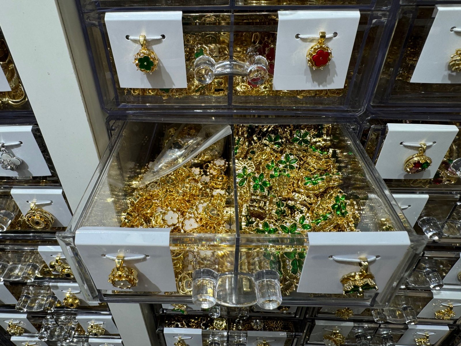 Open drawer with green rhinestone clover charms and white flower frames in gold-plated copper, Yiwu wholesale jewelry findings.