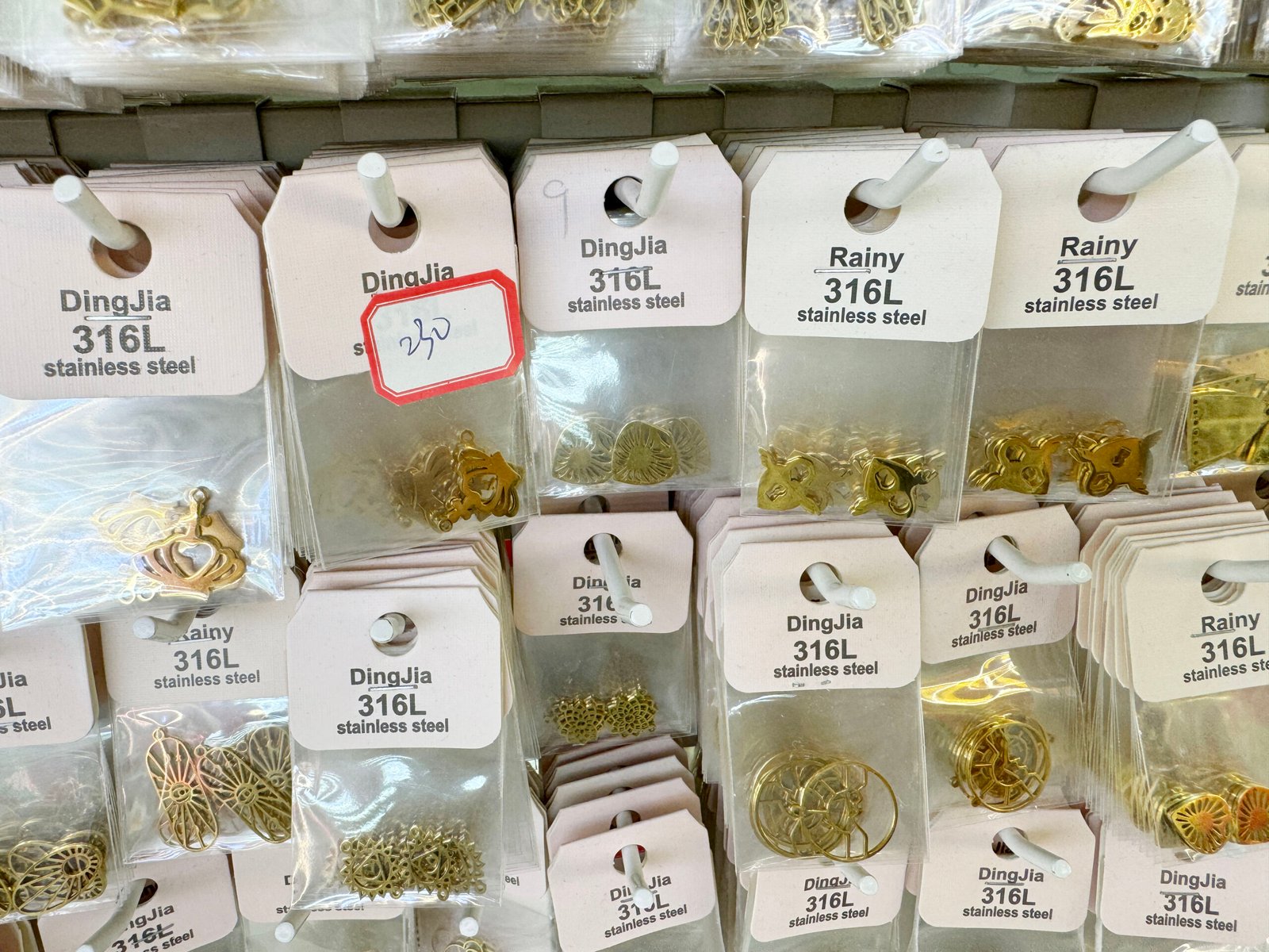 Packets of gold-colored 316L stainless steel charms and geometric connectors hanging on a sample board in yiwu market.
