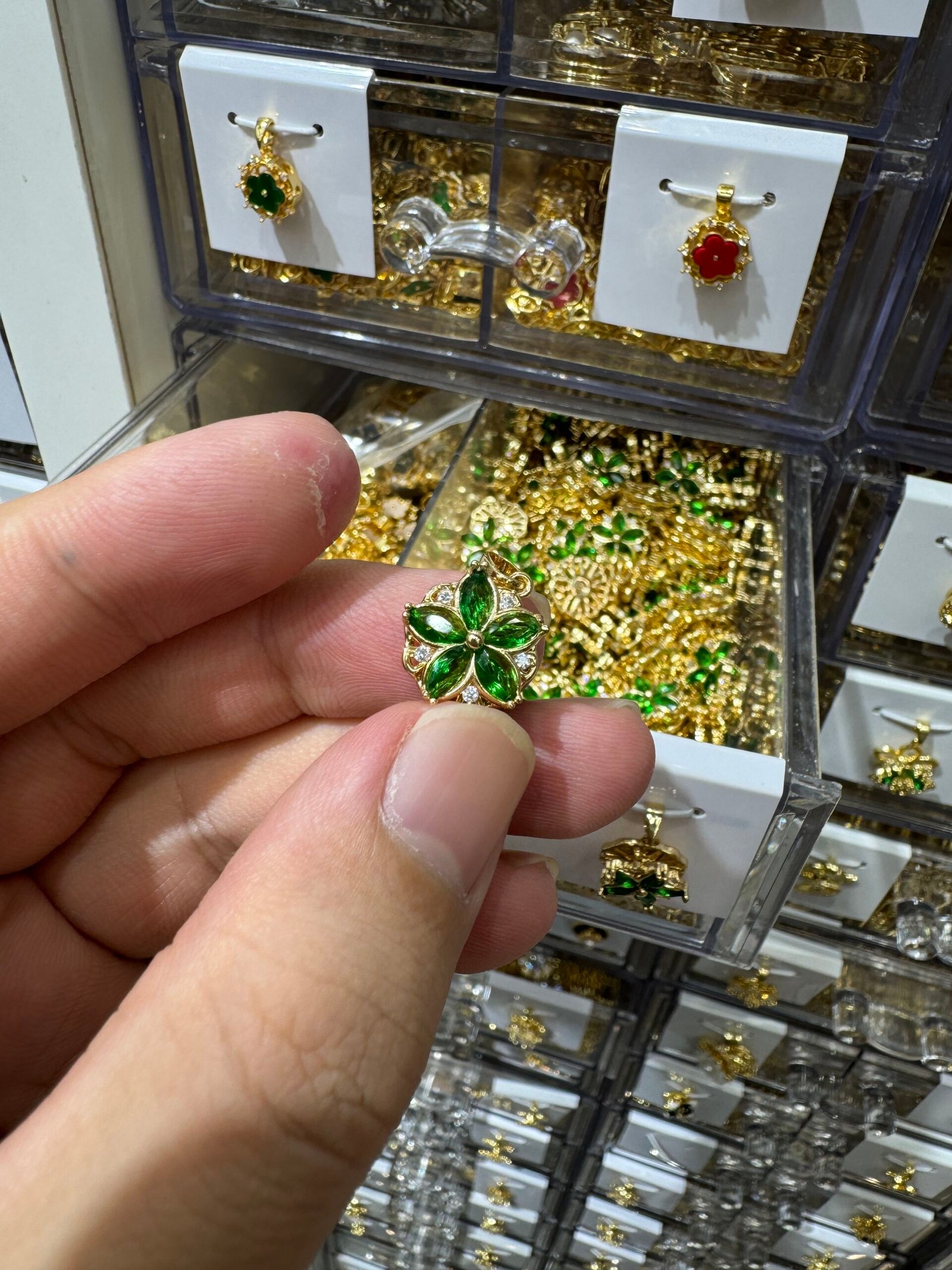 Hand holding green rhinestone five-petal flower pendant with micro-pave stones, gold-plated copper charm from Yiwu supplier.