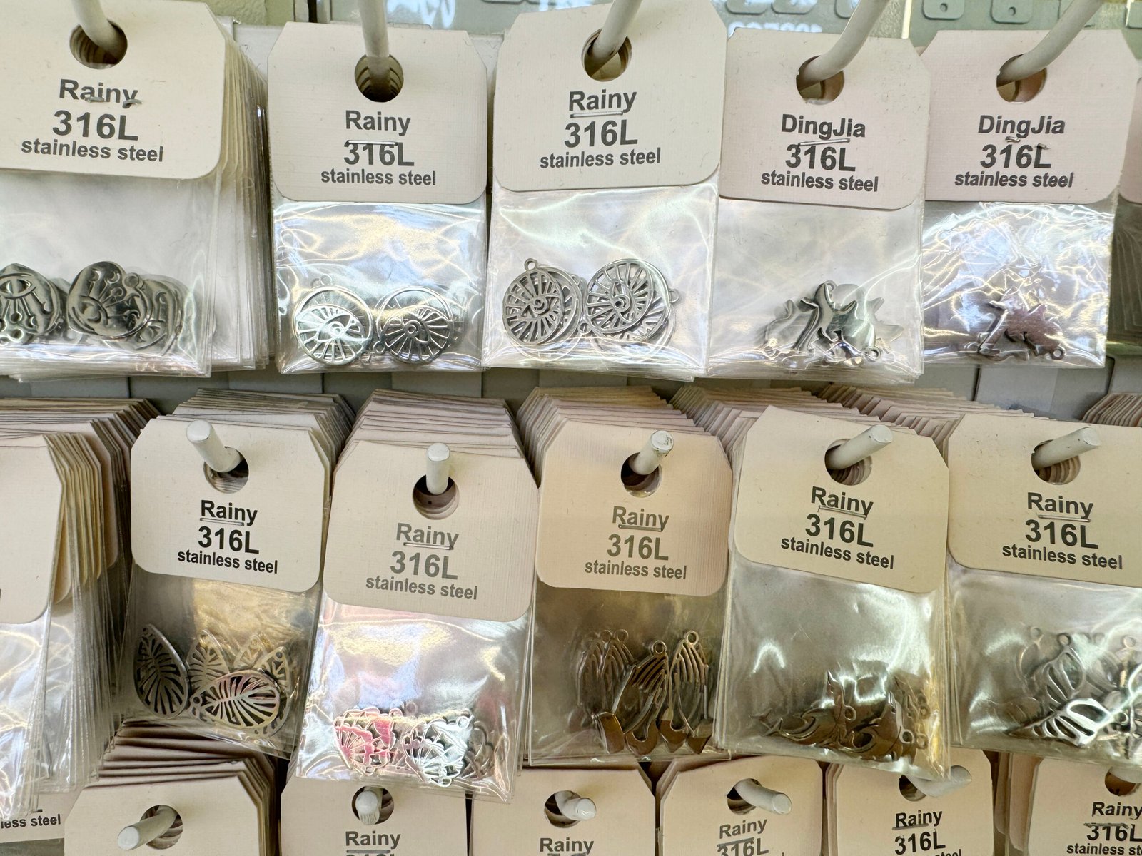 Silver 316L stainless steel disc charms, leaf/butterfly connectors and multi-hole links in packets on hooks.
