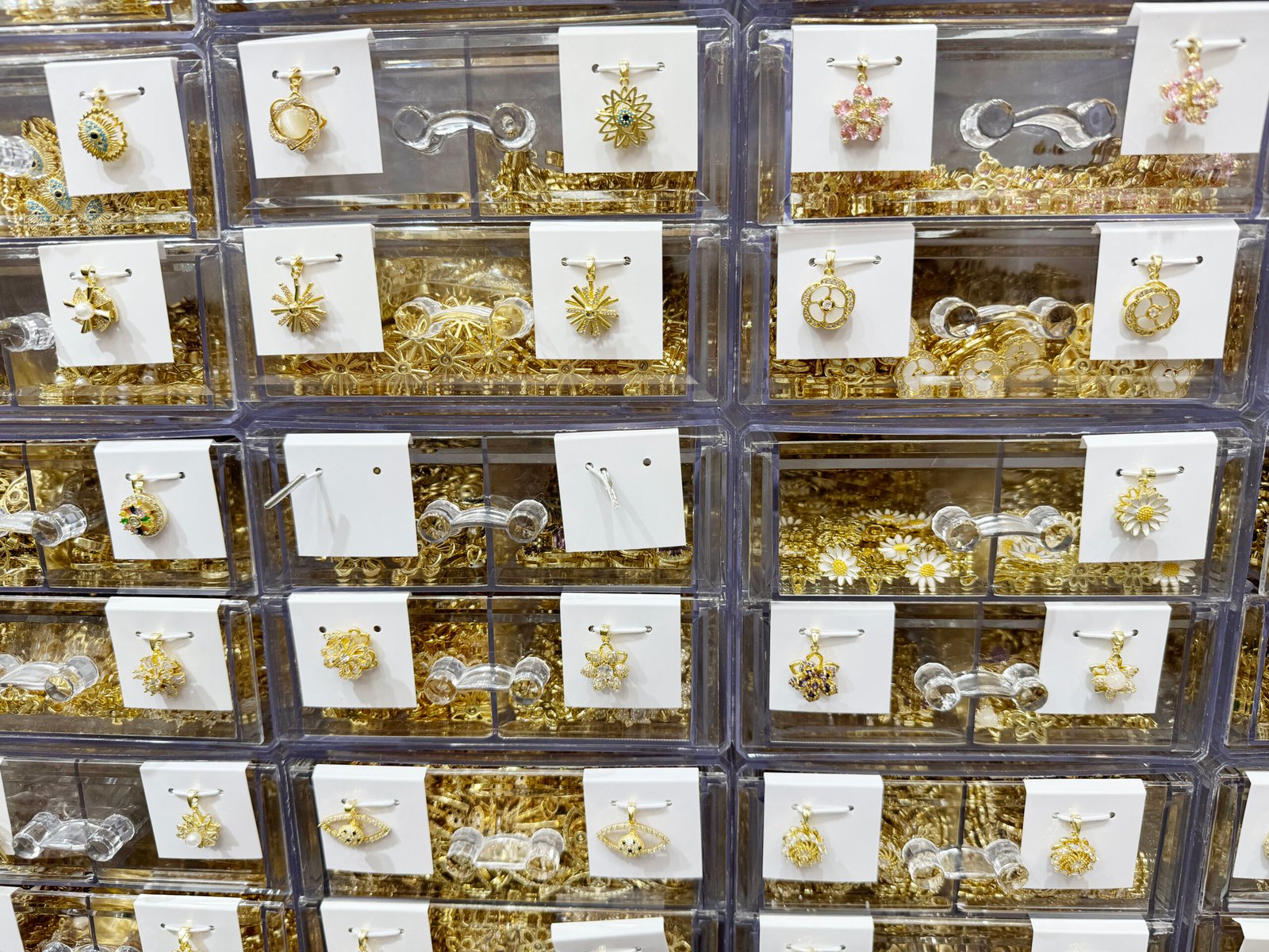 Assorted gold-plated copper charms: sunburst, sakura, enamel daisy, bee and clover designs in Yiwu wholesale showroom.