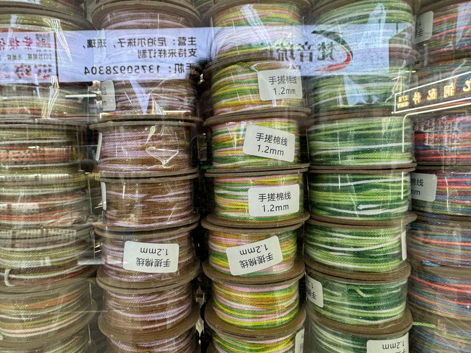 Close view of 1.2 mm multicolor hand-braided cotton cord spools labeled in Chinese at Yiwu accessories market.