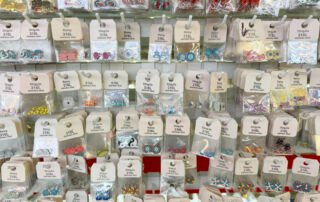 Rows of bagged 316L stainless steel enamel charms and connectors on hooks at a Yiwu supplier sample wall.