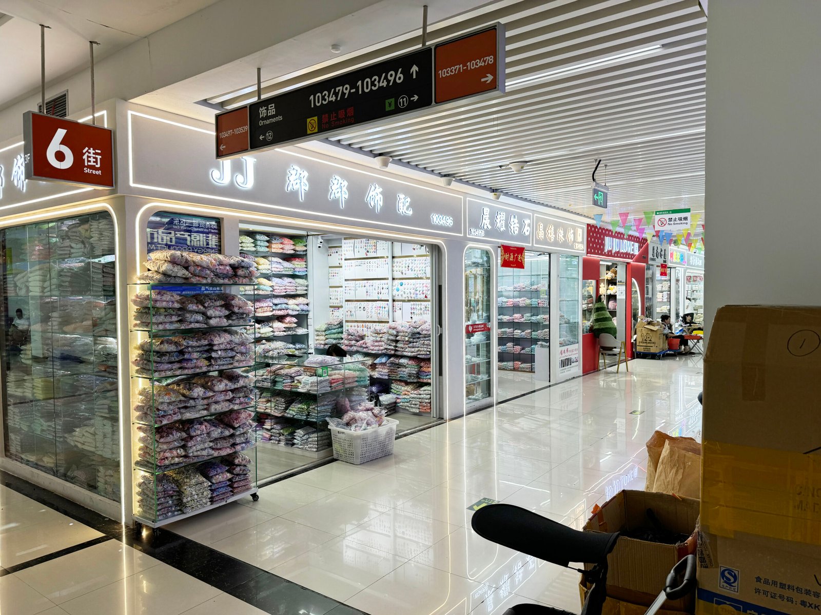 Corner view of Aisle 6 at Yiwu International Trade City showing wholesale ornament shops with shelves of packaged beads, appliqués and trims.