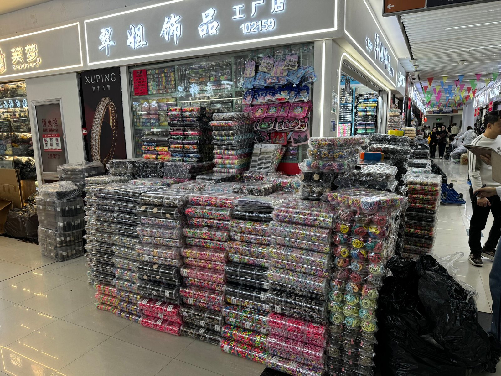 Booth 102159 in Yiwu ornament accessories market with high stacks of packaged elastic hair ties and colorful bands for wholesale.