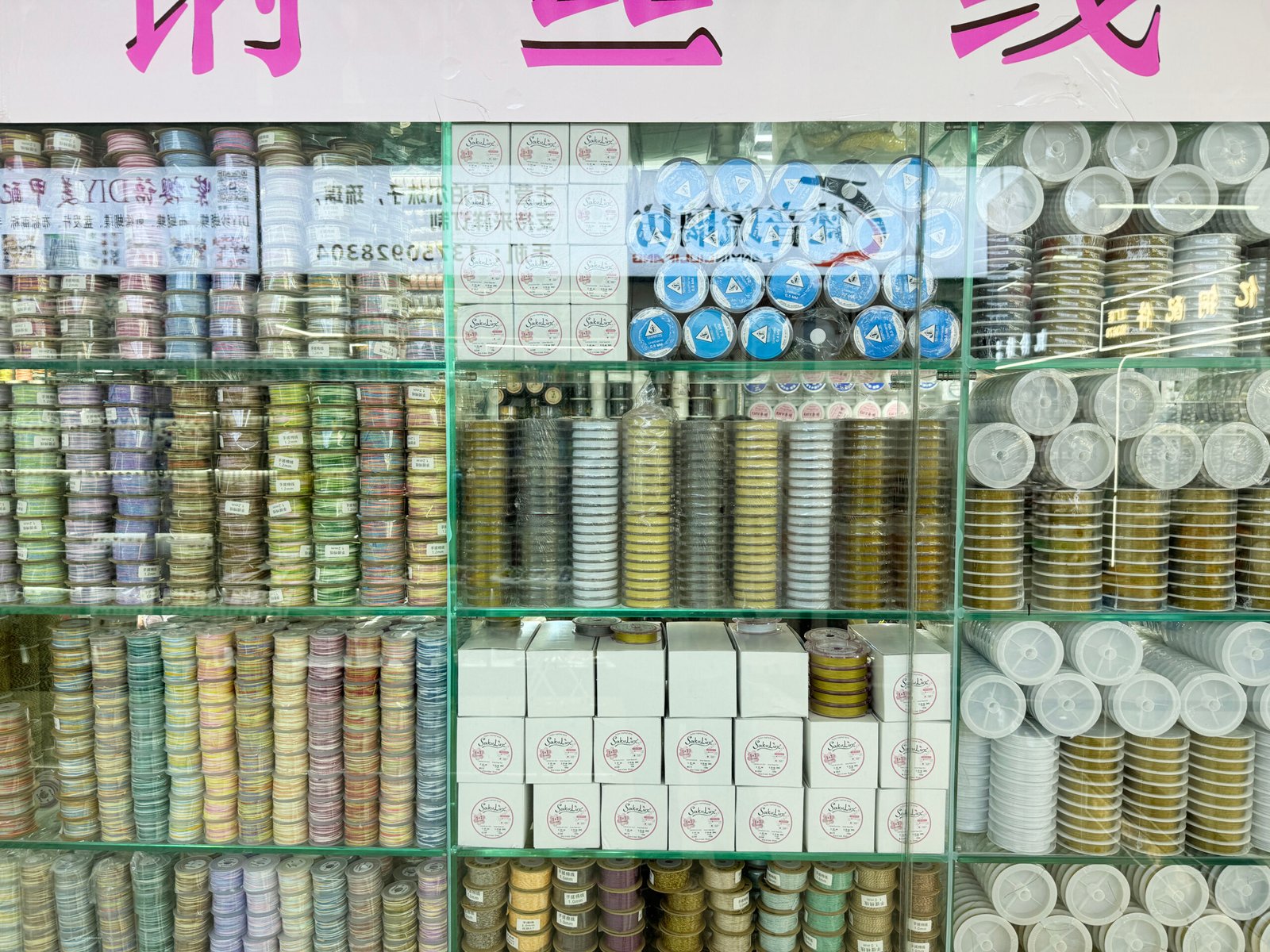 Wall of stacked spools with colored cords, stretch string and metal beading wire at Yiwu accessories market.
