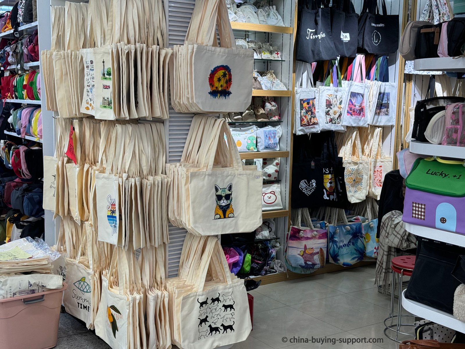 Display of printed canvas tote bags and eco-friendly shopping bags at a supplier shop in Yiwu International Trade City District 2 Gift Packaging Market, showing various custom designs, colors, and sizes for wholesale export.