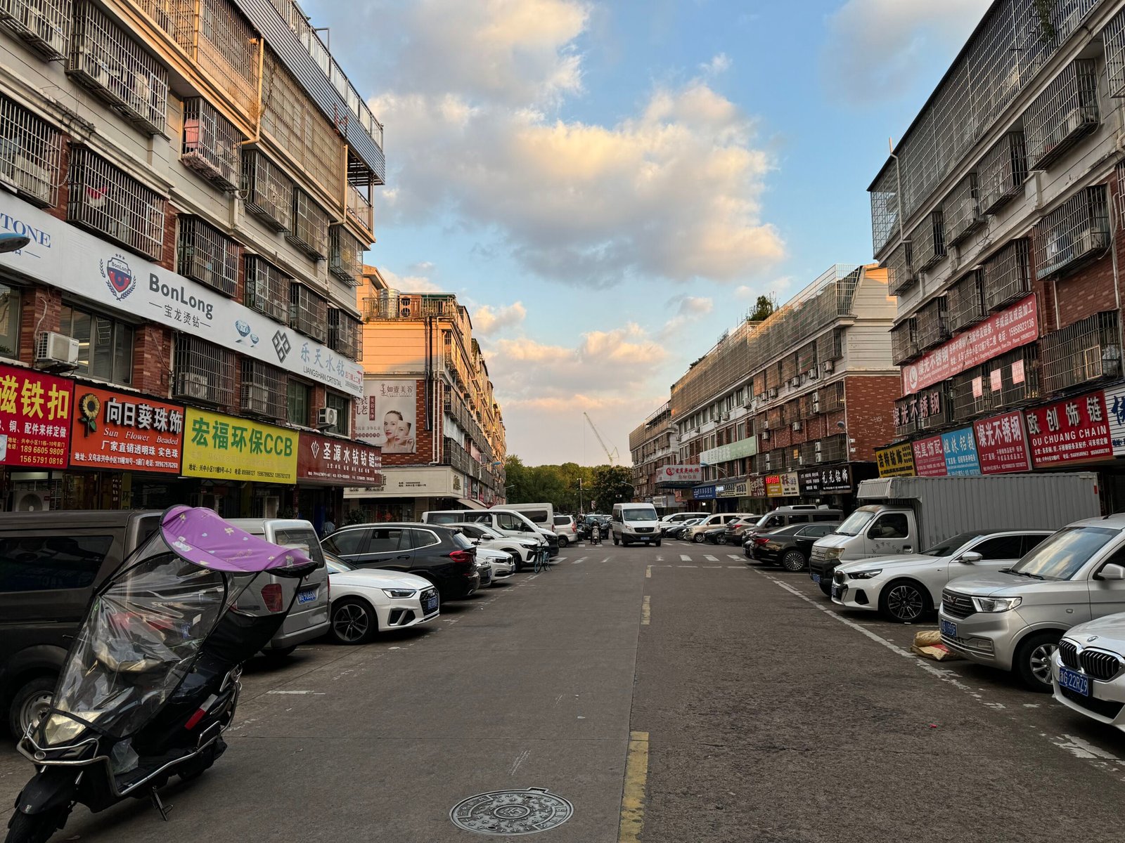 Yiwu Xingzhong accessories street showing stores advertising CCB plastic beads and acrylic jewelry parts with cars and vendors along the street.
