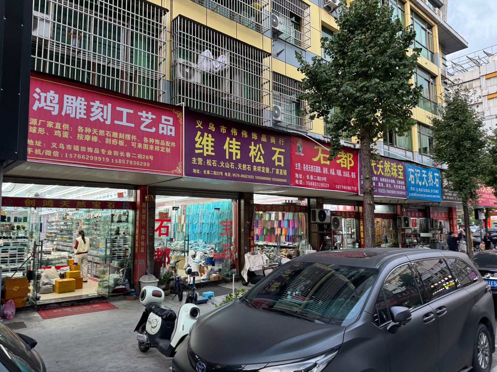 Multiple gemstone stores along Yiwu Changchun Jewelry Accessories Street with strands of turquoise, lava rock, agate, jade; showcases of carved beads, pendants, connectors and cords. Photographed in Yiwu China