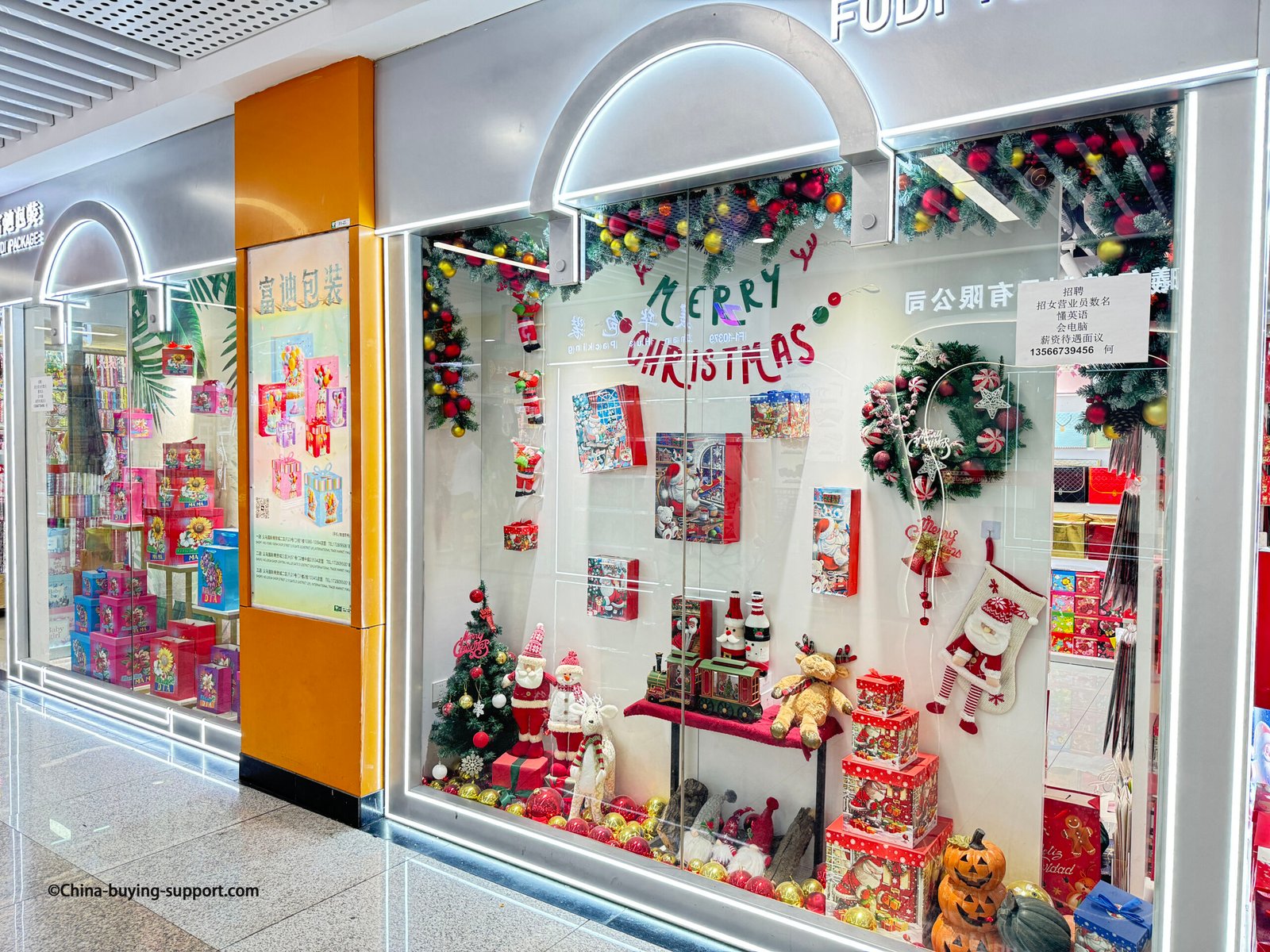Christmas-themed gift packaging display at Yiwu International Trade City Zone 2, featuring festive boxes, Santa Claus figures, holiday wrapping, and decorative wreaths from a Chinese supplier.