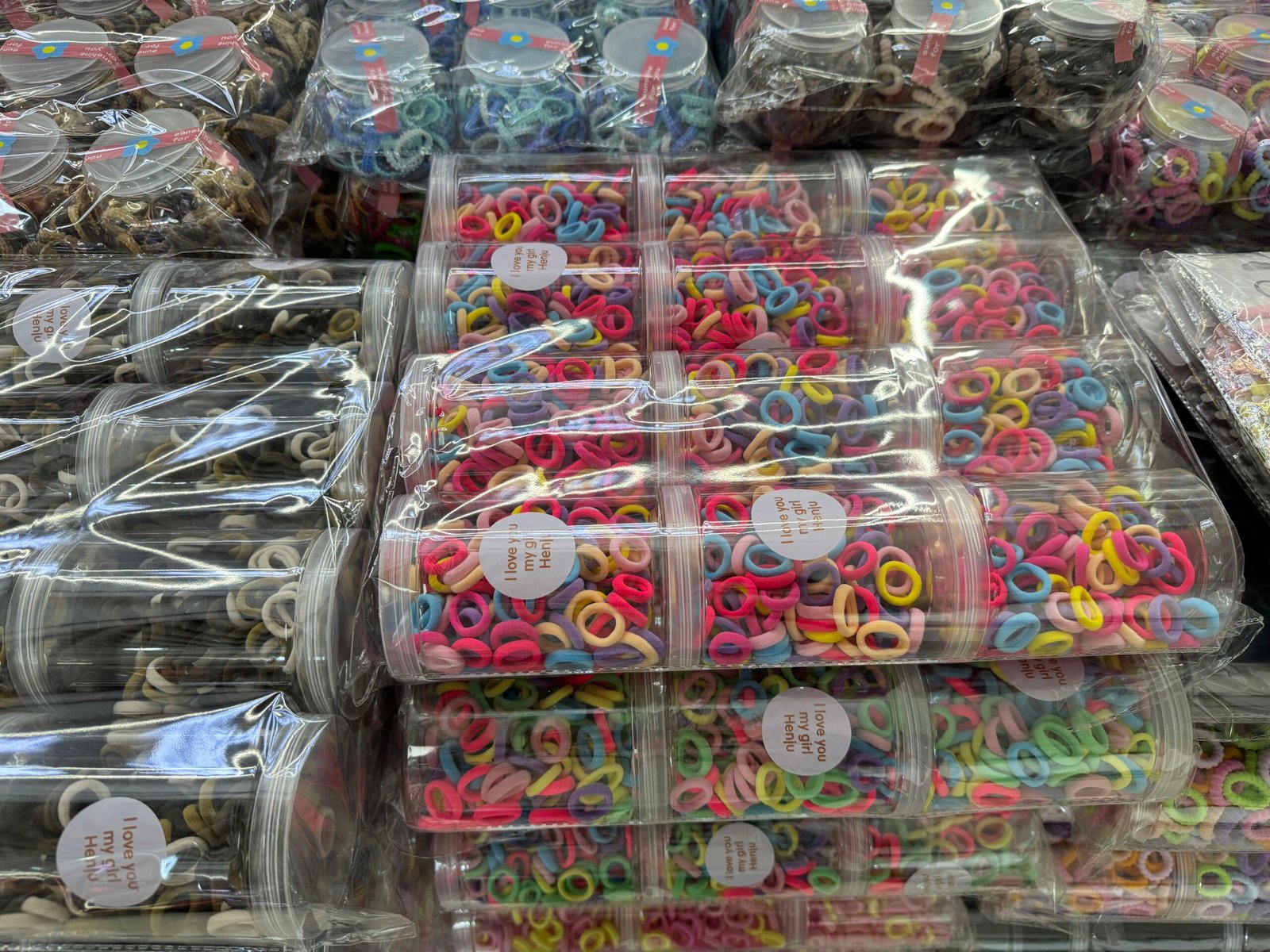 Close view of jars filled with bright mini elastic hair bands under shrink wrap, labeled for retail, at Yiwu hair accessories wholesale market.