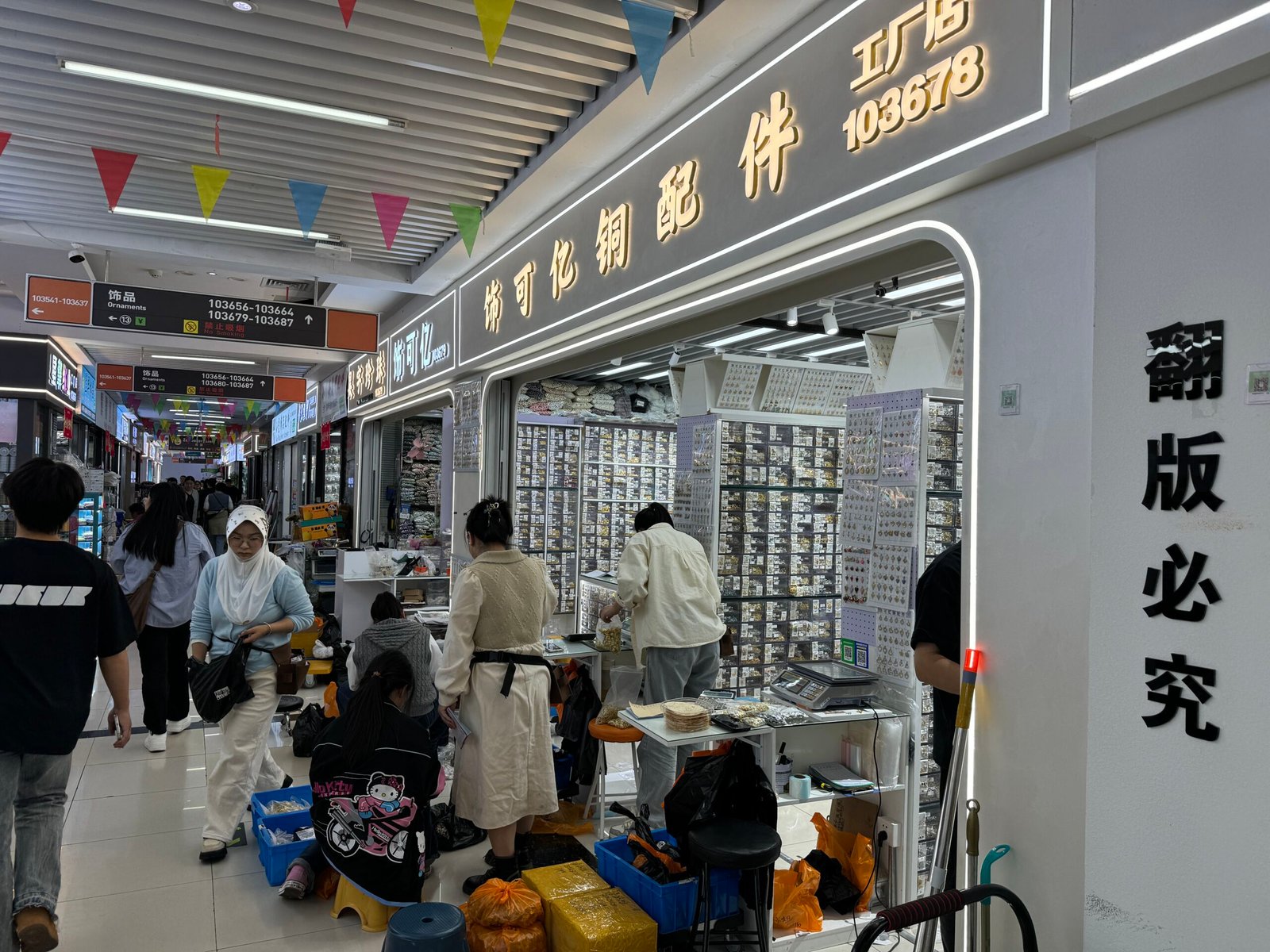 Yiwu Trade City Area 1 East aisle with copper jewelry findings shop 103678 and wall displays of pendants, earring parts and beads.