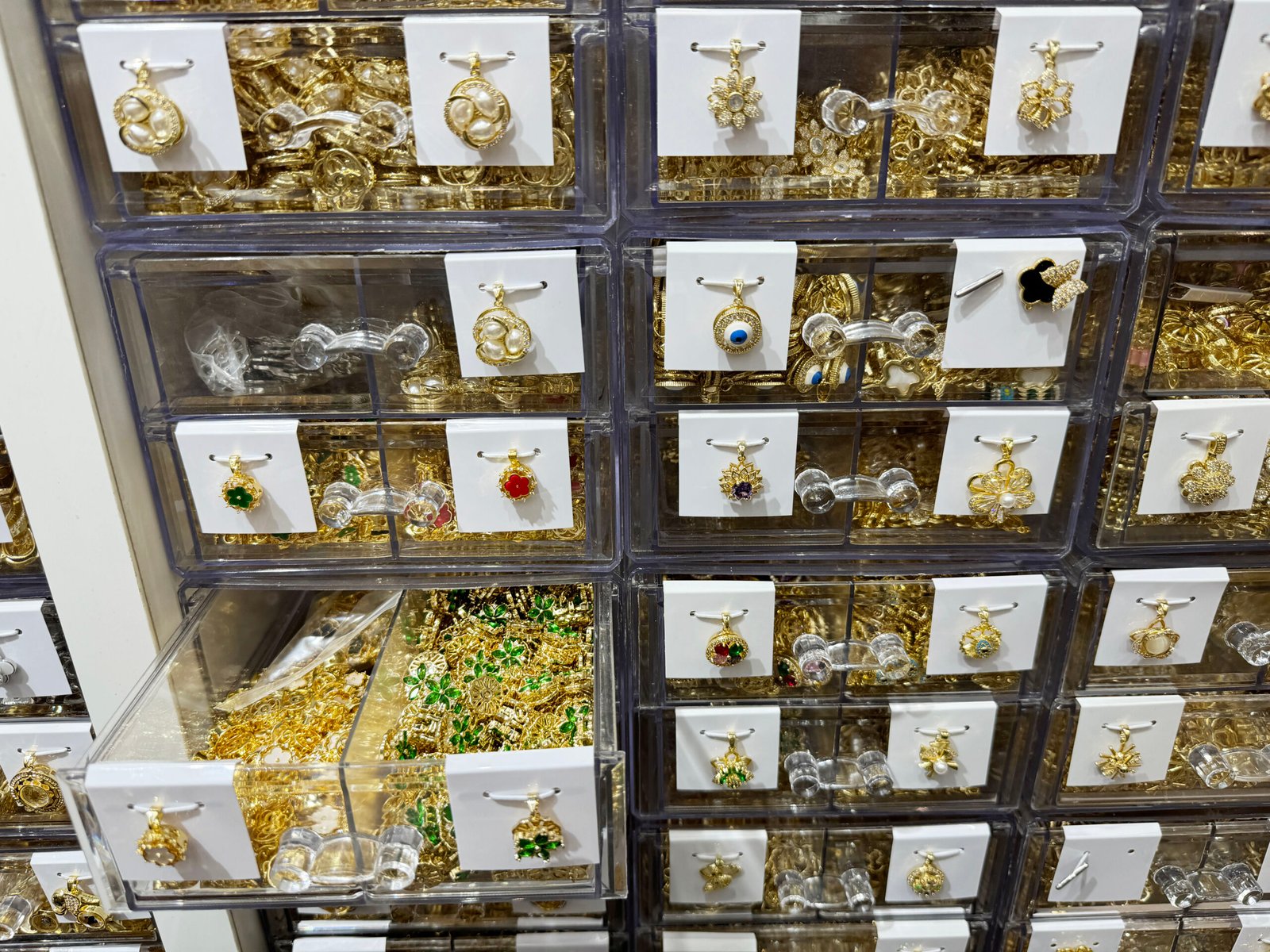 Wall of drawers with gold-plated copper pendant charms in Yiwu—flower, clover, evil eye and micro-pave designs for DIY jewelry.