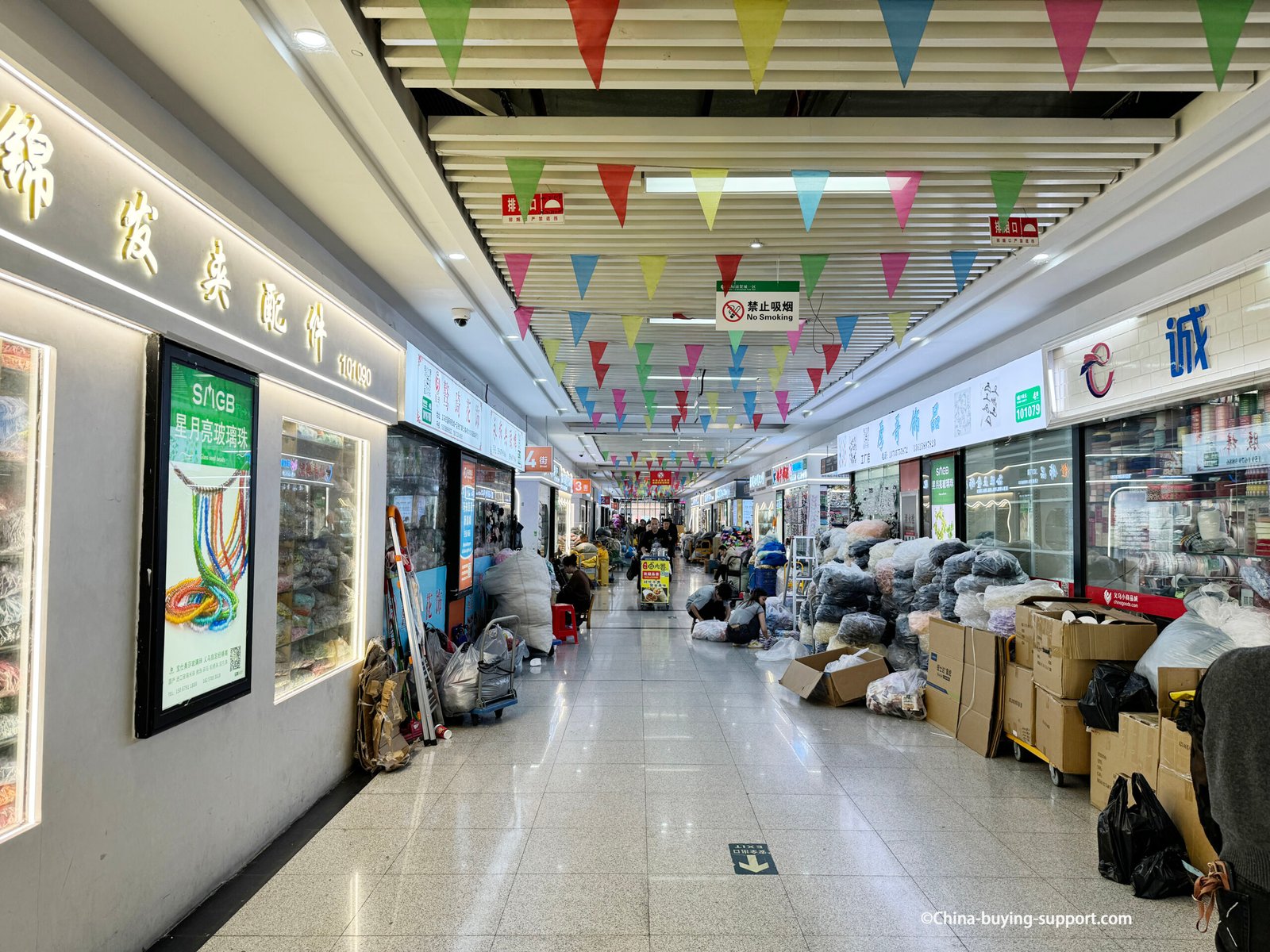 Wide aisle inside Yiwu International Trade City District 1 East Expansion showing jewelry accessory shops, stacked cartons and bags