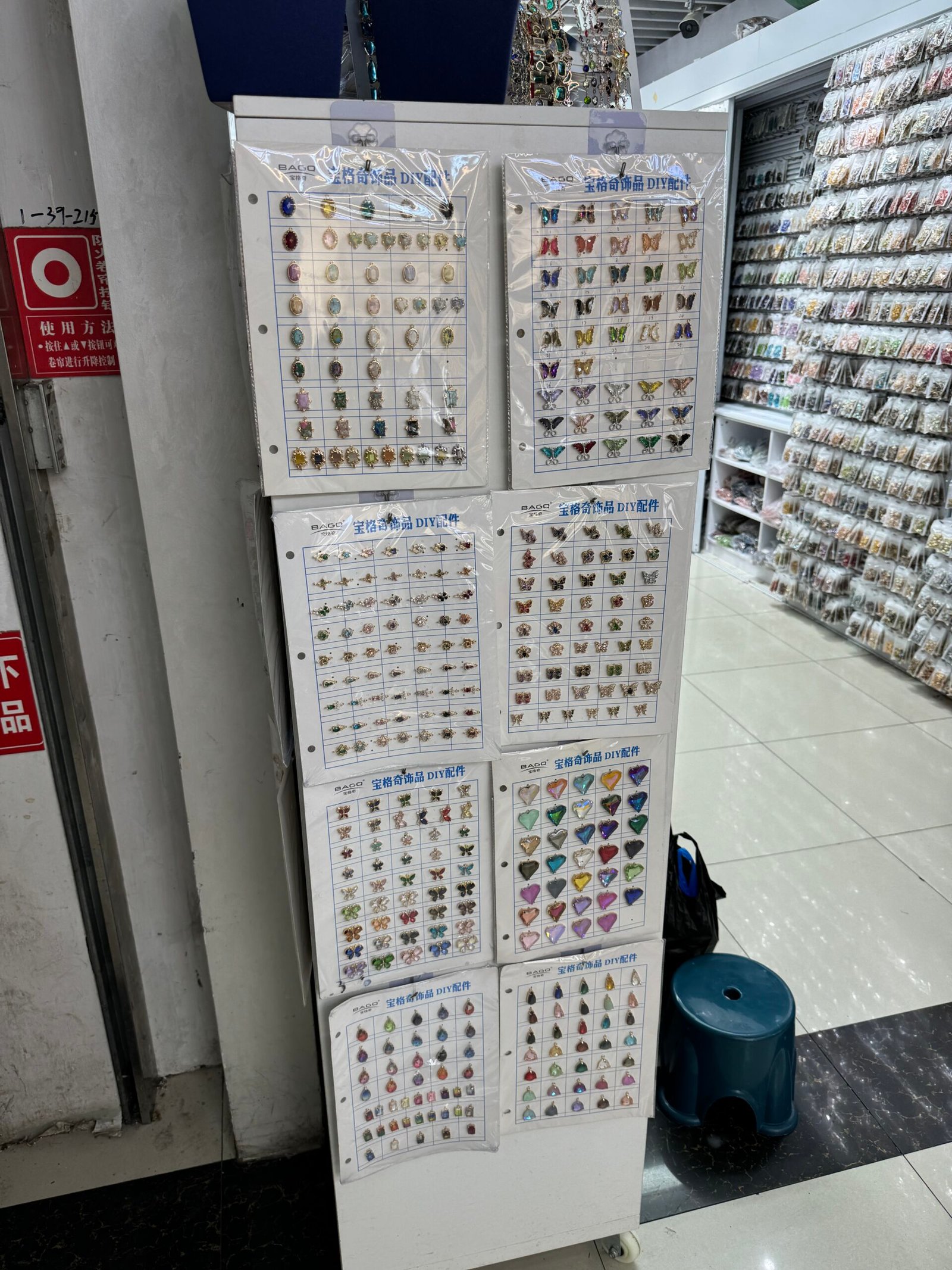 Close view of sample boards displaying assorted butterfly, heart, star and gem-style pendants for DIY jewelry inside a Yiwu accessories wholesale shop.