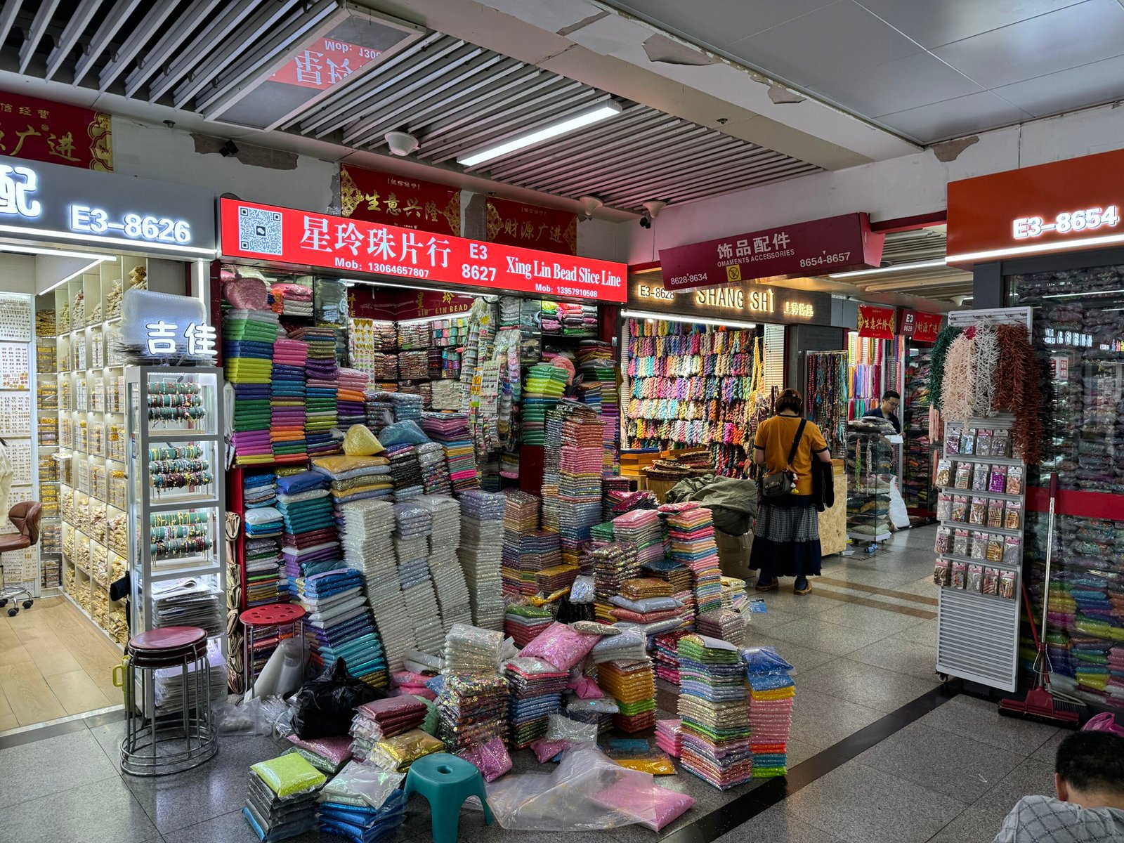 Yiwu E Area shop E3-8627 with stacked sequin sheets and glitter packs for bulk wholesale.