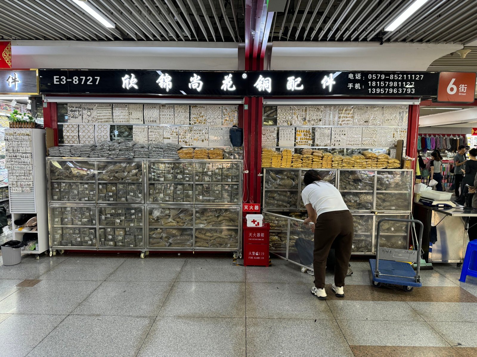 Storefront E3-8727 stacked with bagged brass findings—jump rings, hoops, pendant bails—in Yiwu Market 3rd Floor, E Area.