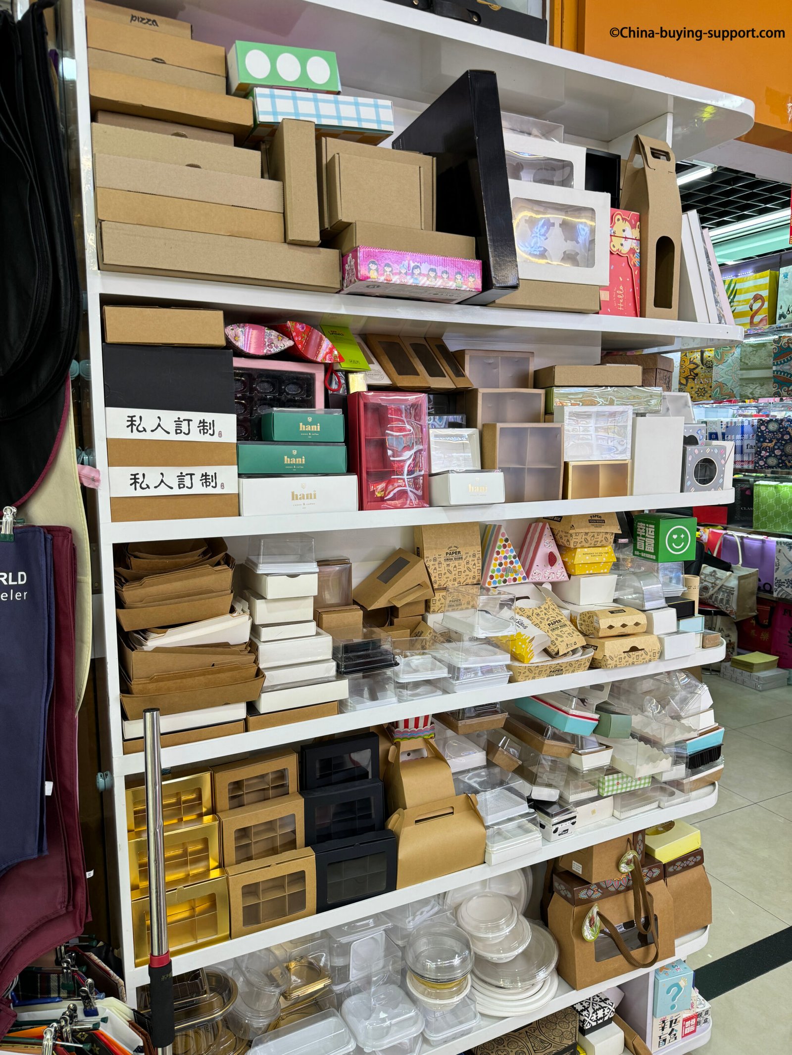 Shelves filled with various food packaging boxes including kraft paper boxes, plastic containers, and custom printed packaging on display at a supplier shop in Yiwu International Trade City District 2, China.