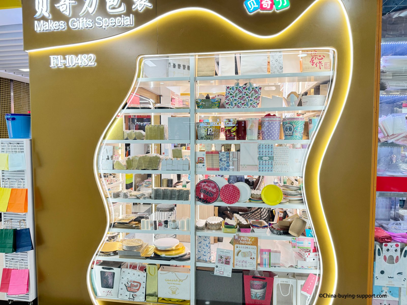 Display window of a food packaging supplier in Yiwu International Trade City District 2 showing paper cups, popcorn buckets, cake boxes, and disposable tableware for bakery and party use.