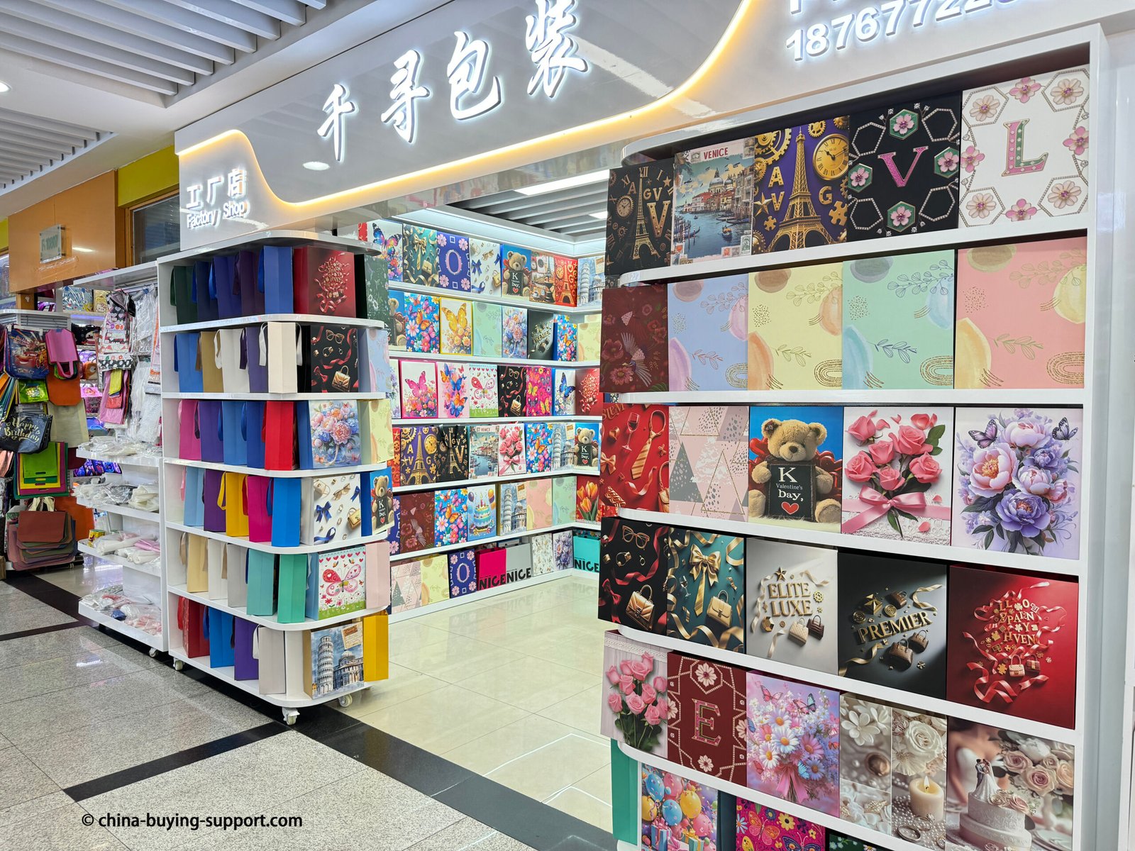 Front view of a colorful gift bag supplier shop in Yiwu International Trade City, featuring decorative paper bags and luxury packaging designs displayed on shelves