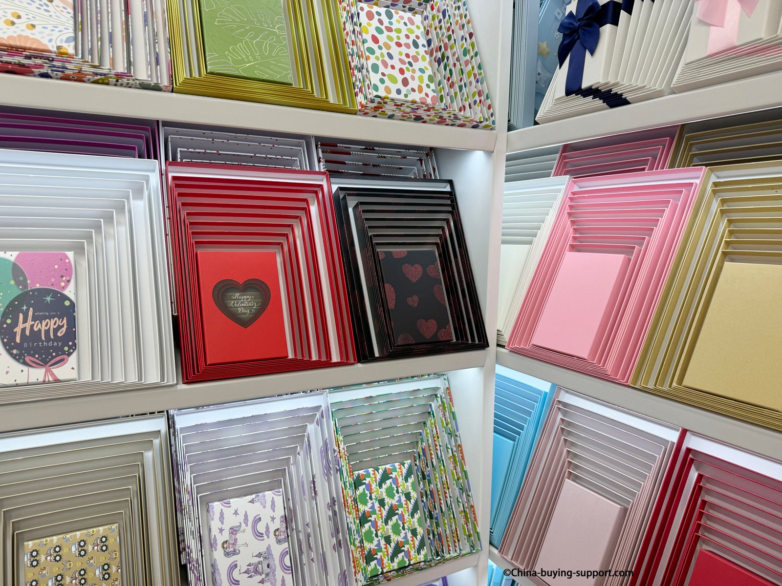 Ten-piece colorful gift box sets displayed on shelves at a Yiwu International Trade City Zone 2 supplier shop, showing nesting boxes in red, pink, black, and gold for retail and gift packaging.