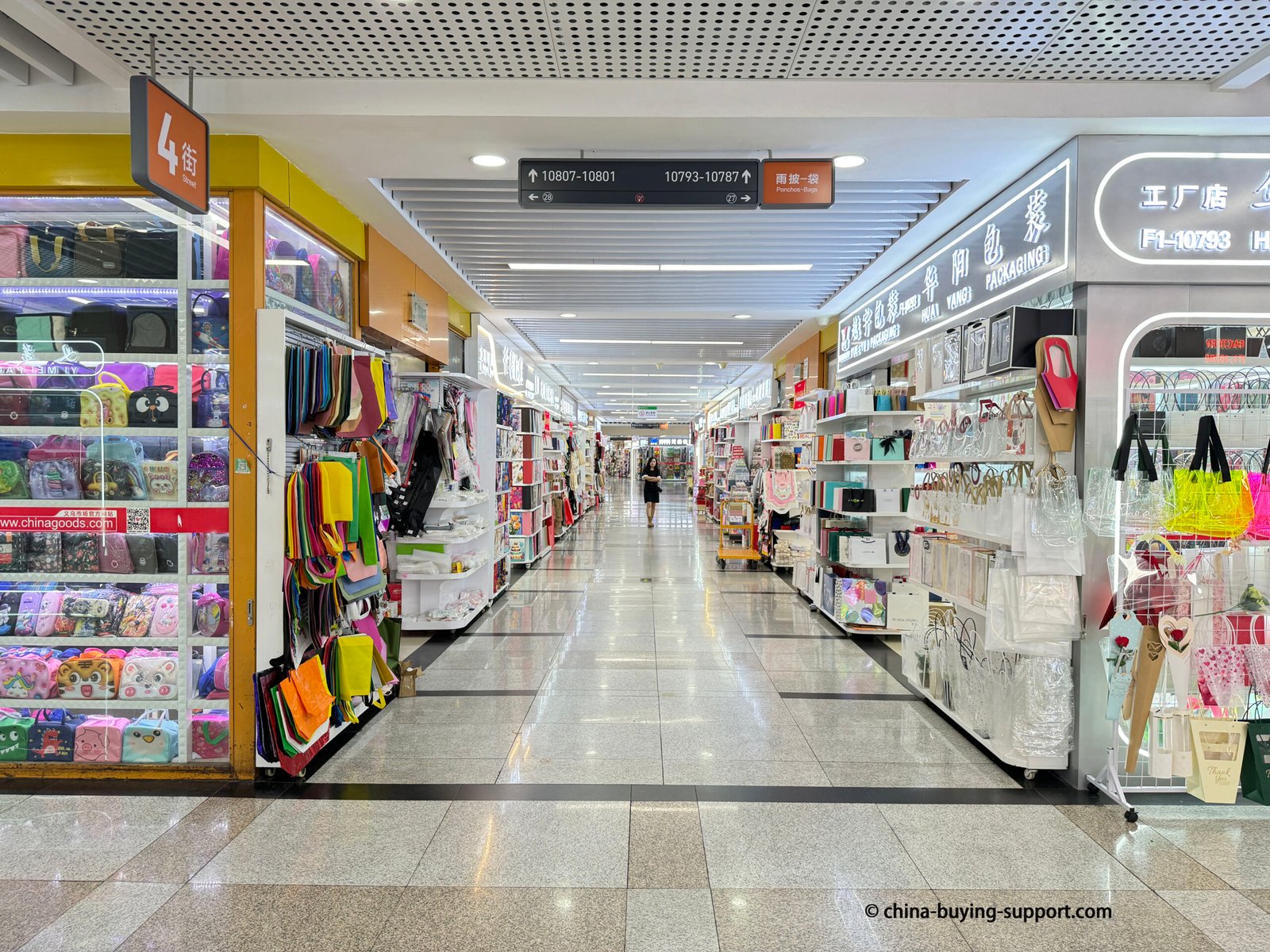 Interior of Yiwu International Trade City District 2 in China, showing gift packaging market shops with displays of paper bags, gift boxes, and non-woven bags for wholesale buyers.