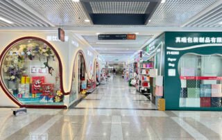 Gift packaging and paper bag supplier corridor inside Yiwu International Trade City District 2, showing colorful packaging stores offering paper bags, gift boxes, and wrapping products for wholesale buyers.