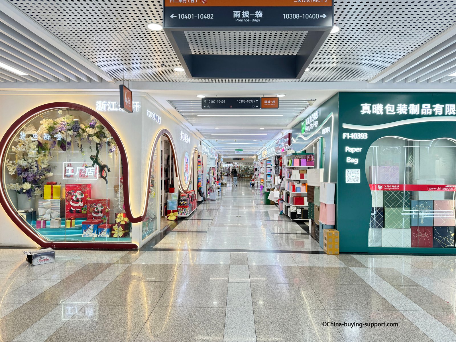 Gift packaging and paper bag supplier corridor inside Yiwu International Trade City District 2, showing colorful packaging stores offering paper bags, gift boxes, and wrapping products for wholesale buyers.