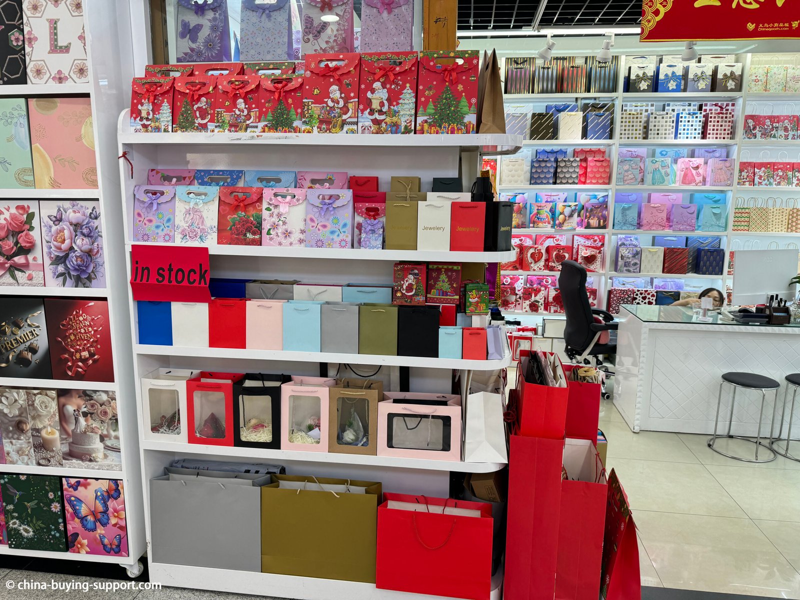 Display shelves of a gift packaging supplier shop at Yiwu International Trade City District 2, China, showing colorful paper gift bags, holiday designs, and luxury packaging boxes for wholesale buyers.