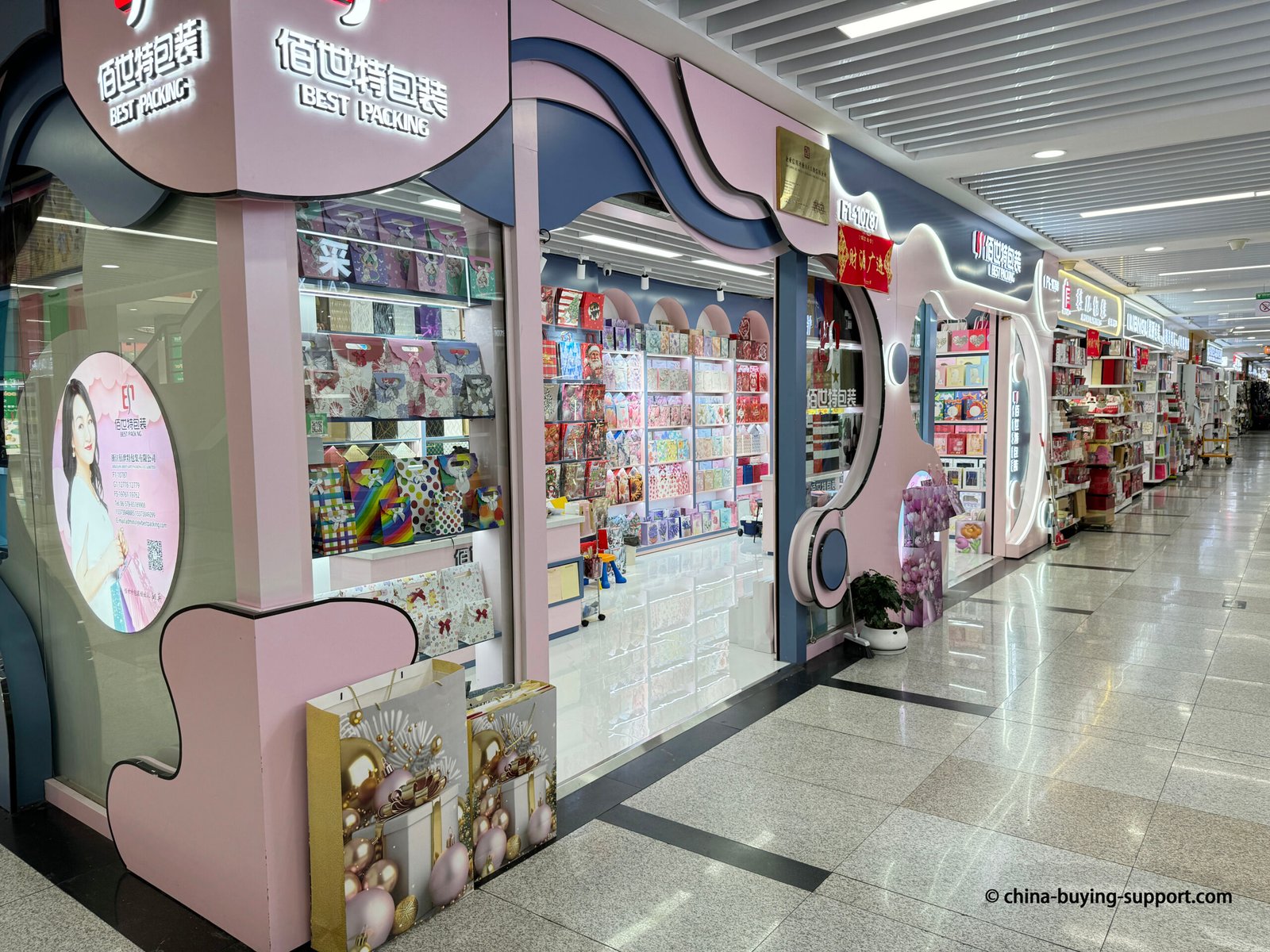 Storefront of a gift paper bag supplier in Yiwu International Trade City District 2, China, displaying colorful printed paper bags, luxury wrapping papers, and decorative packaging products for wholesale buyers.