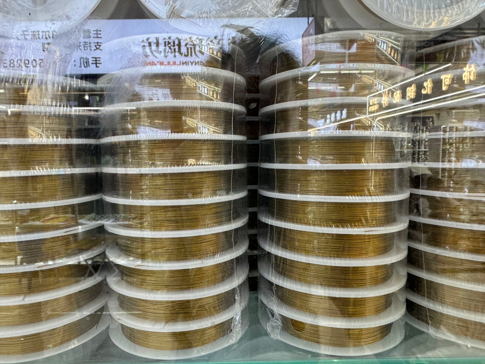 Tall stacks of gold-colored brass jewelry wire spools wrapped in plastic at Yiwu market, China